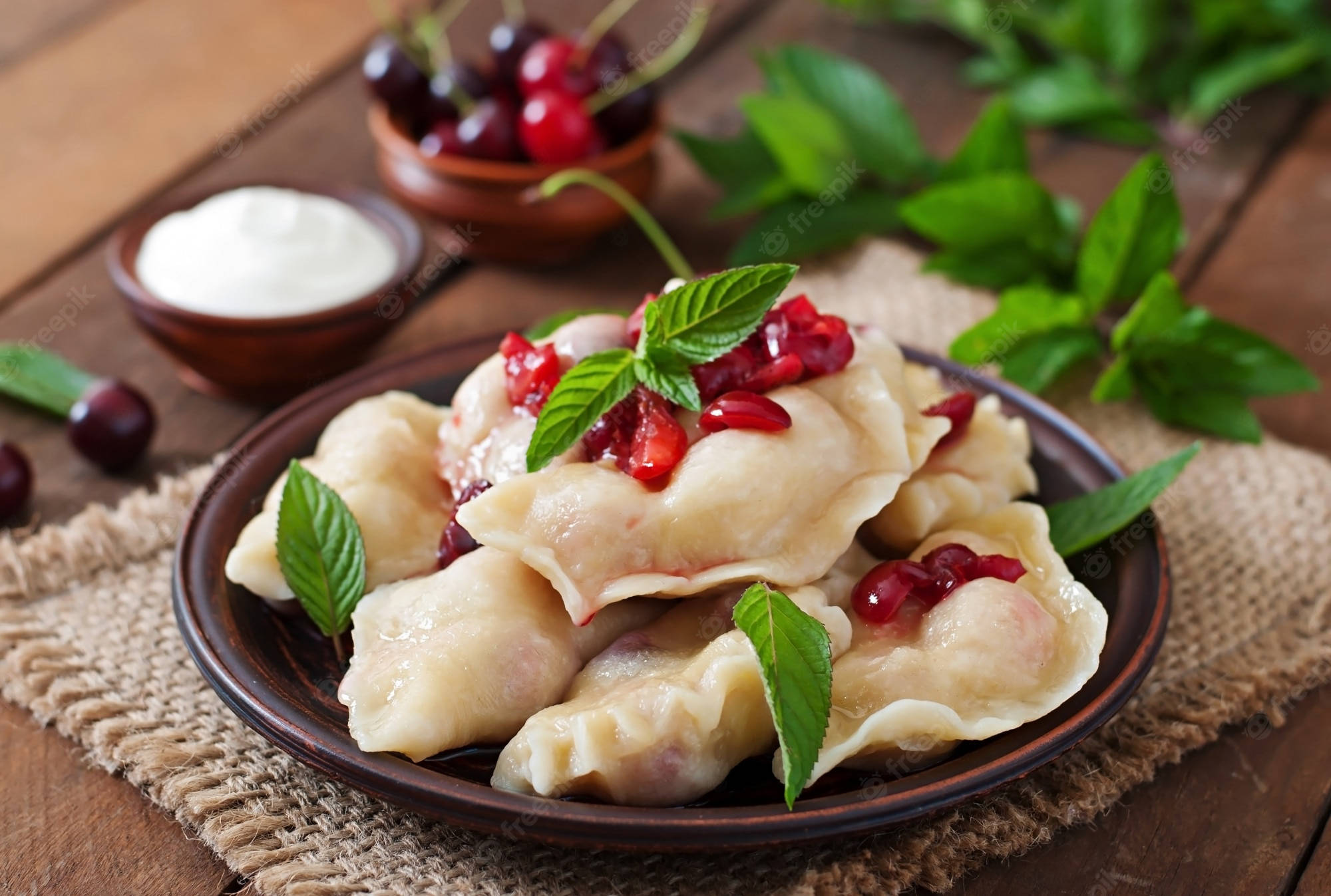 Food Photography 桌布 壁紙 — 蒸餃子上放有石榴籽和薄荷葉，放在質樸的木桌上，搭配櫻桃裝飾和酸奶油。