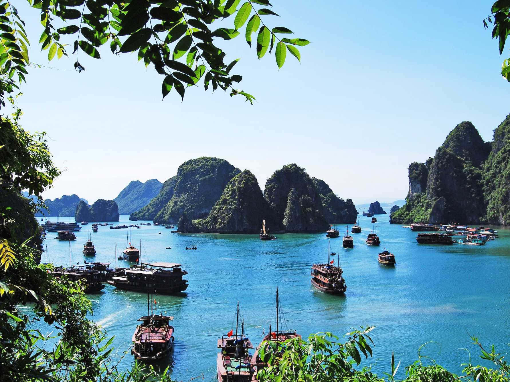 越南 桌布 壁紙 — 蒼翠的喀斯特島嶼從碧綠色的海水中升起，海面上點綴著傳統木船，天空清澈湛藍。