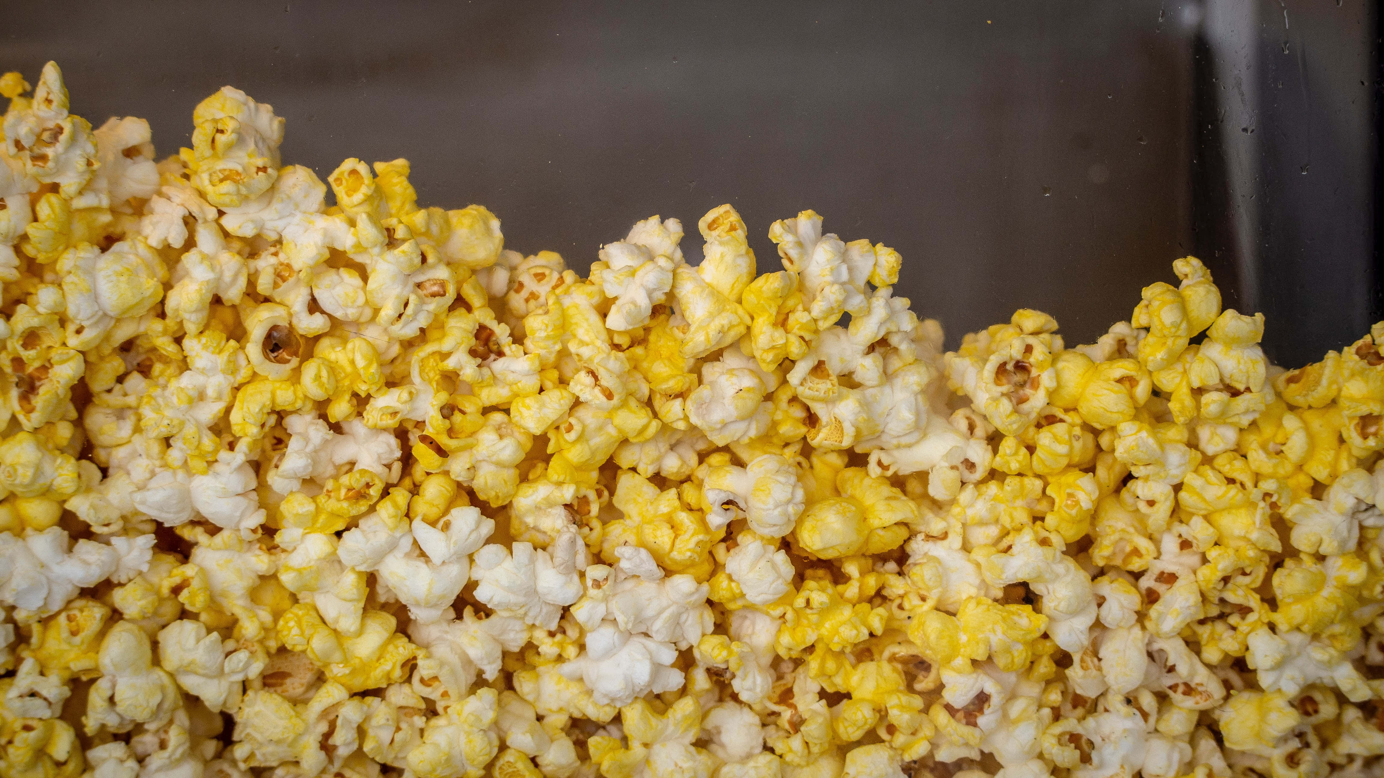 Popcorn 桌布 壁紙 — 蓬鬆黃白爆米花粒溢出深色表面的特寫。