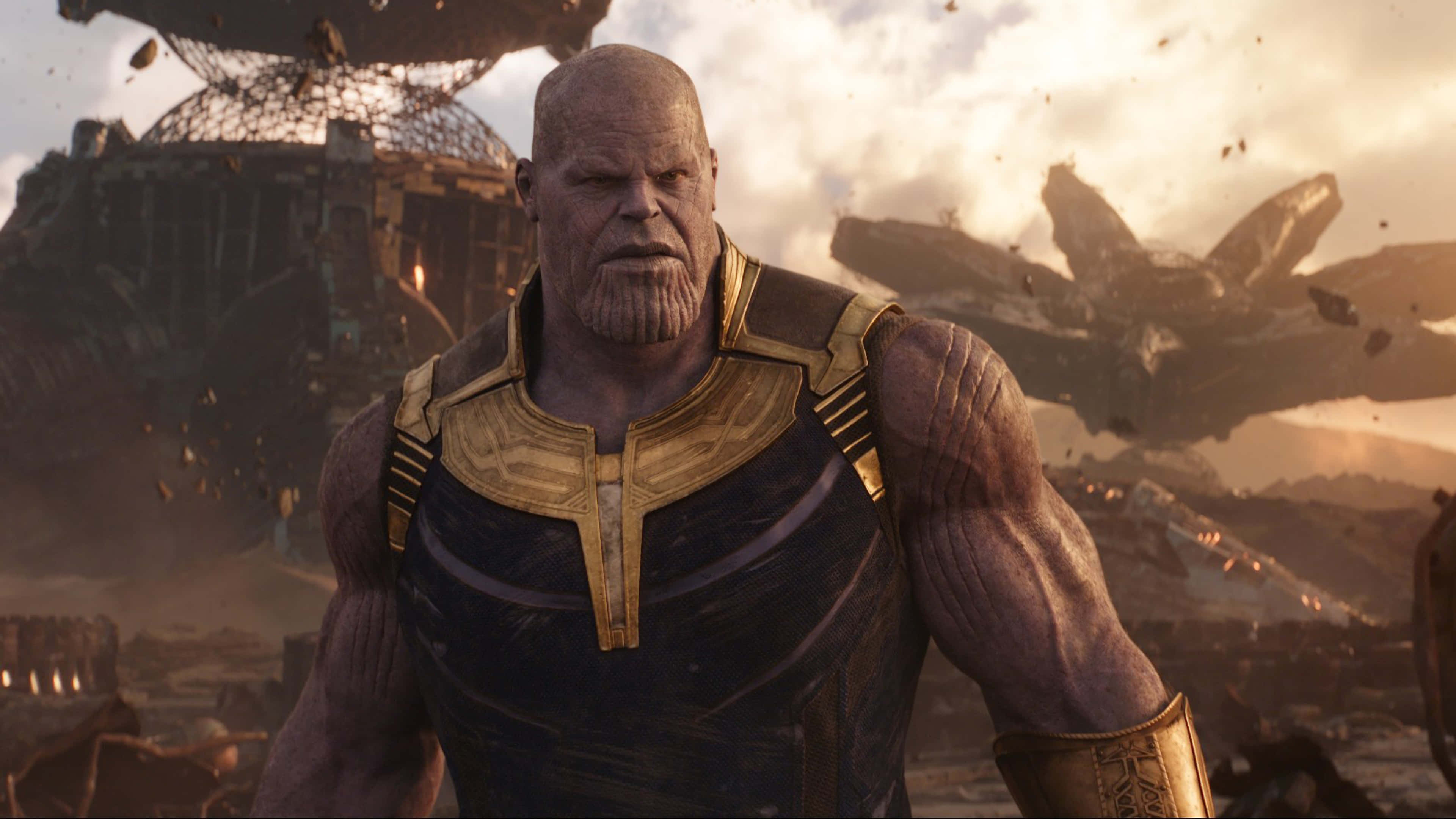 infinity war 桌布 壁紙 — 薩諾斯威嚴地站在一個被戰爭摧毀的戰場上，周圍是破碎的船隻和崩塌的建築物，天空燃燒著火焰。