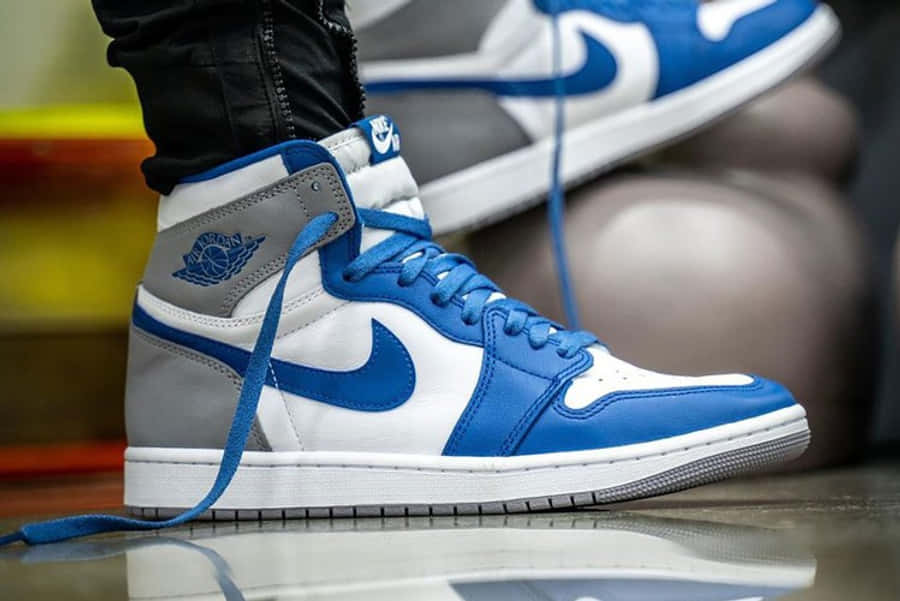 鞋子 桌布 壁紙 — 藍白灰色Jordan 1高筒運動鞋特寫，鞋帶未繫，置於反光地板上。