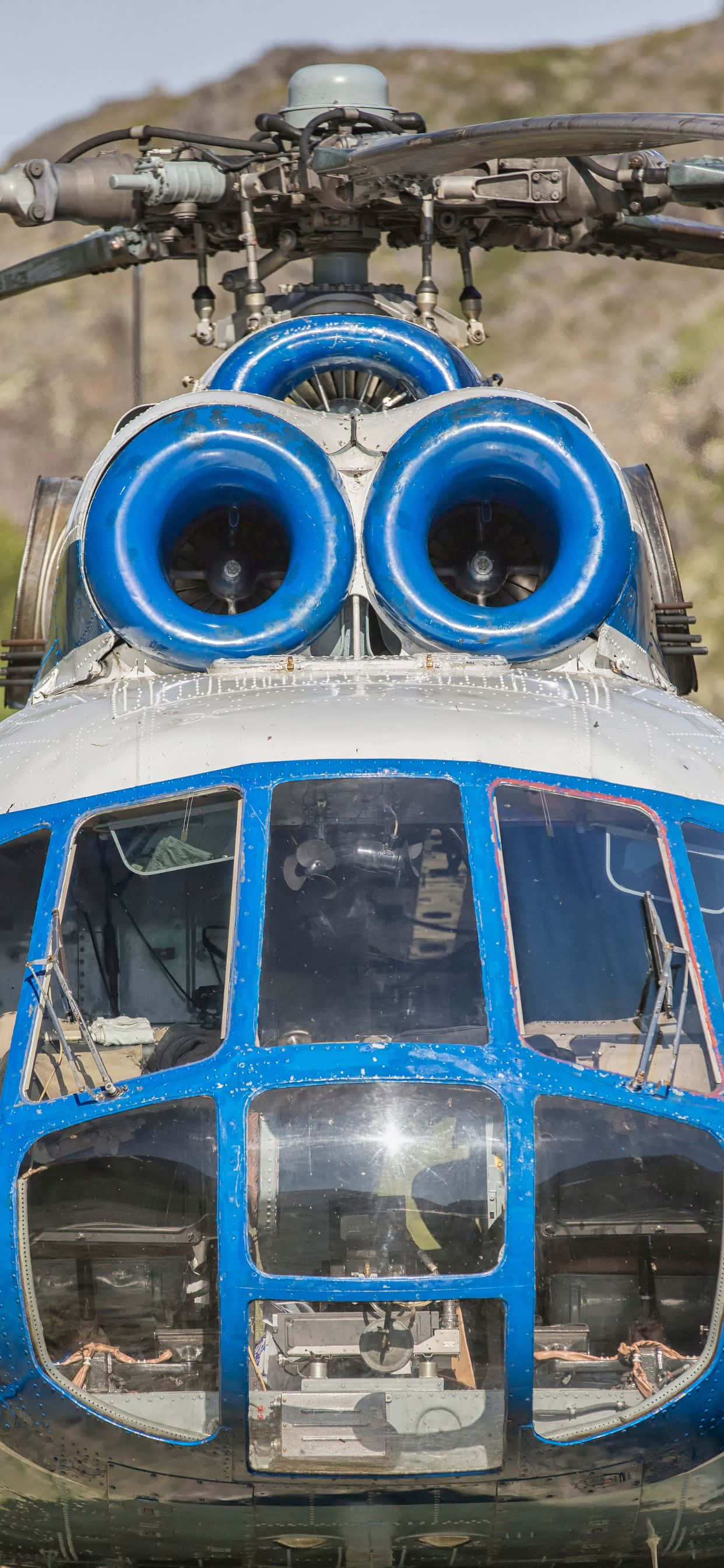 iPhone Xs Max Helicopters 桌布 壁紙 — 藍白直升機駕駛艙及雙引擎在岩石山坡前的特寫。