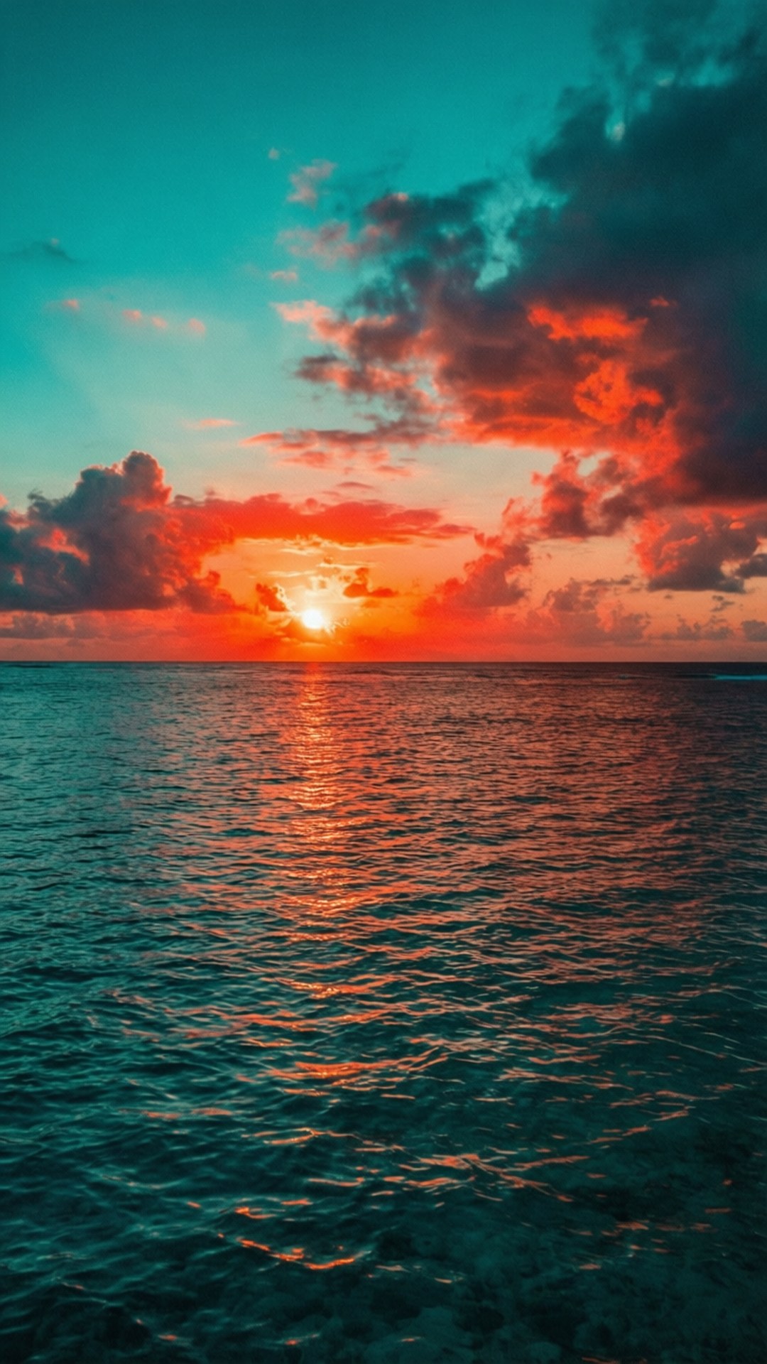 藍綠色珊瑚夕陽 壁紙 — 平靜海面上充滿活力的日落，火紅的橙色雲彩倒映在藍綠色的海面上。
