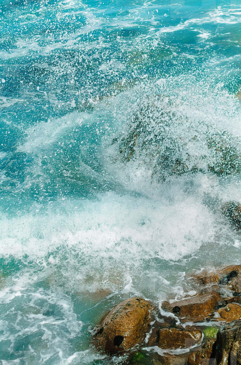 Beautiful Ocean 桌布 壁紙 — 藍綠色的海浪猛烈地拍打著粗糙的棕色岩石，激起白色的泡沫向上飛濺。