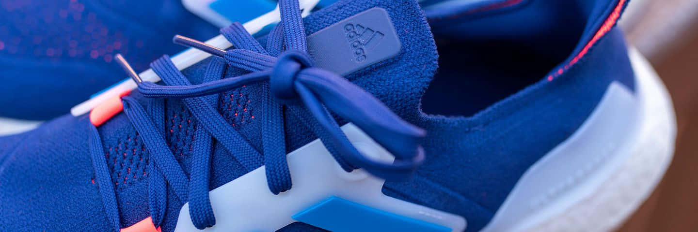 愛迪達 桌布 壁紙 — 藍色 Adidas 運動鞋的特寫，白色鞋底和橙色點綴，展示詳細的鞋帶和紋理布料。