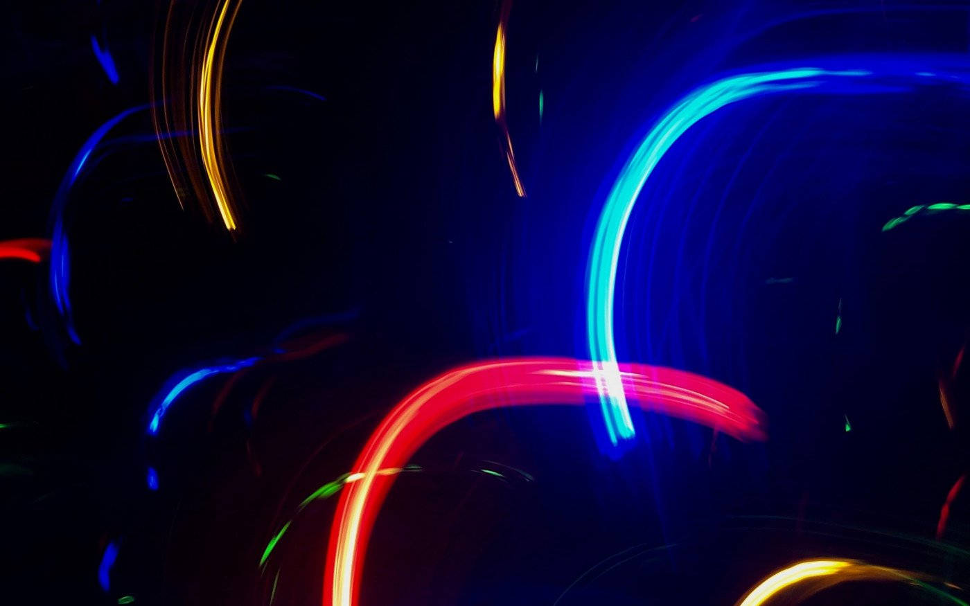 Neon Light 桌布 壁紙 — 藍色、紅色和黃色的鮮豔光條在深黑色背景上動態旋轉。