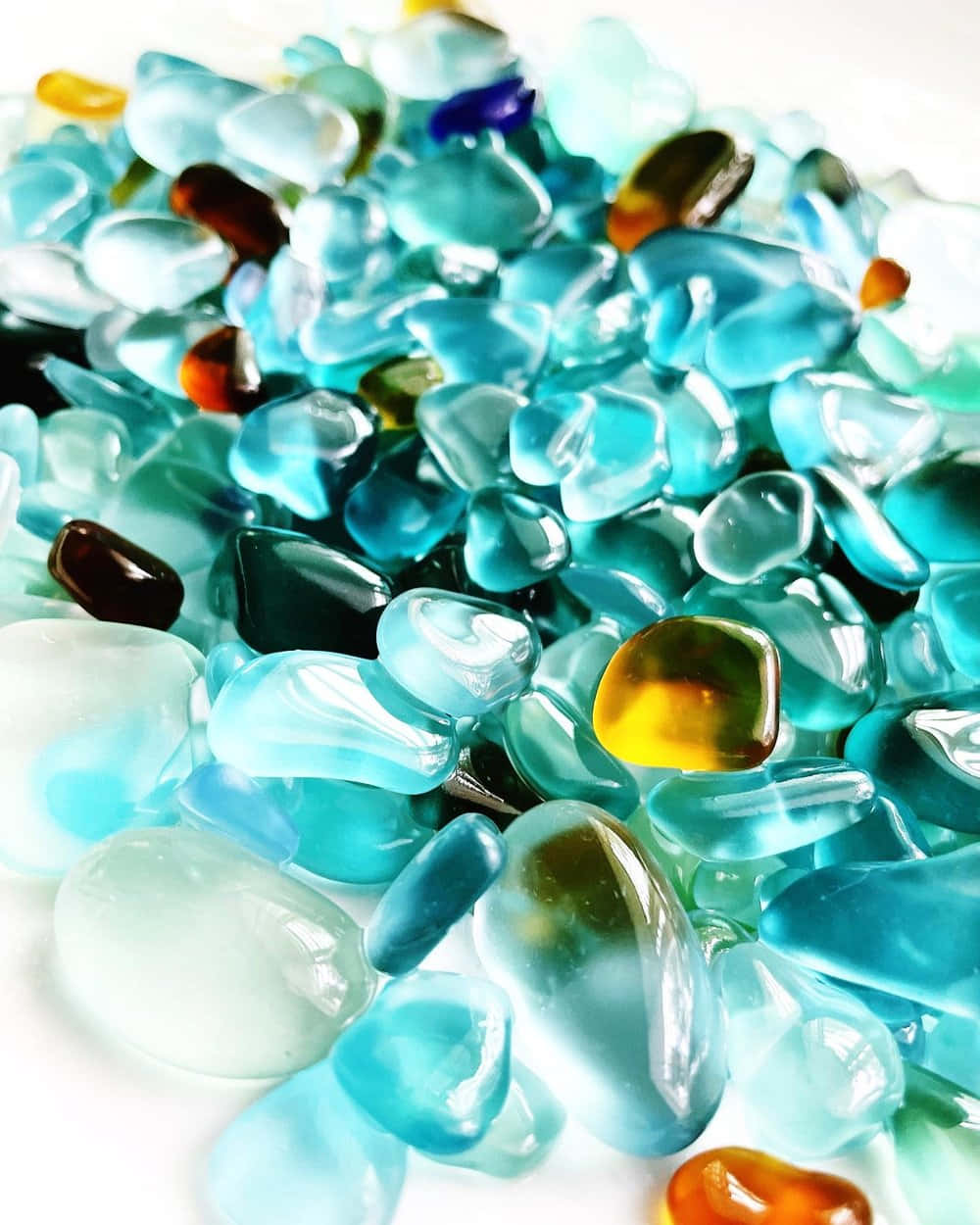 Sea Glass 桌布 壁紙 — 藍色、綠色和琥珀色調的光澤多色玻璃卵石散落在白色表面上的特寫。
