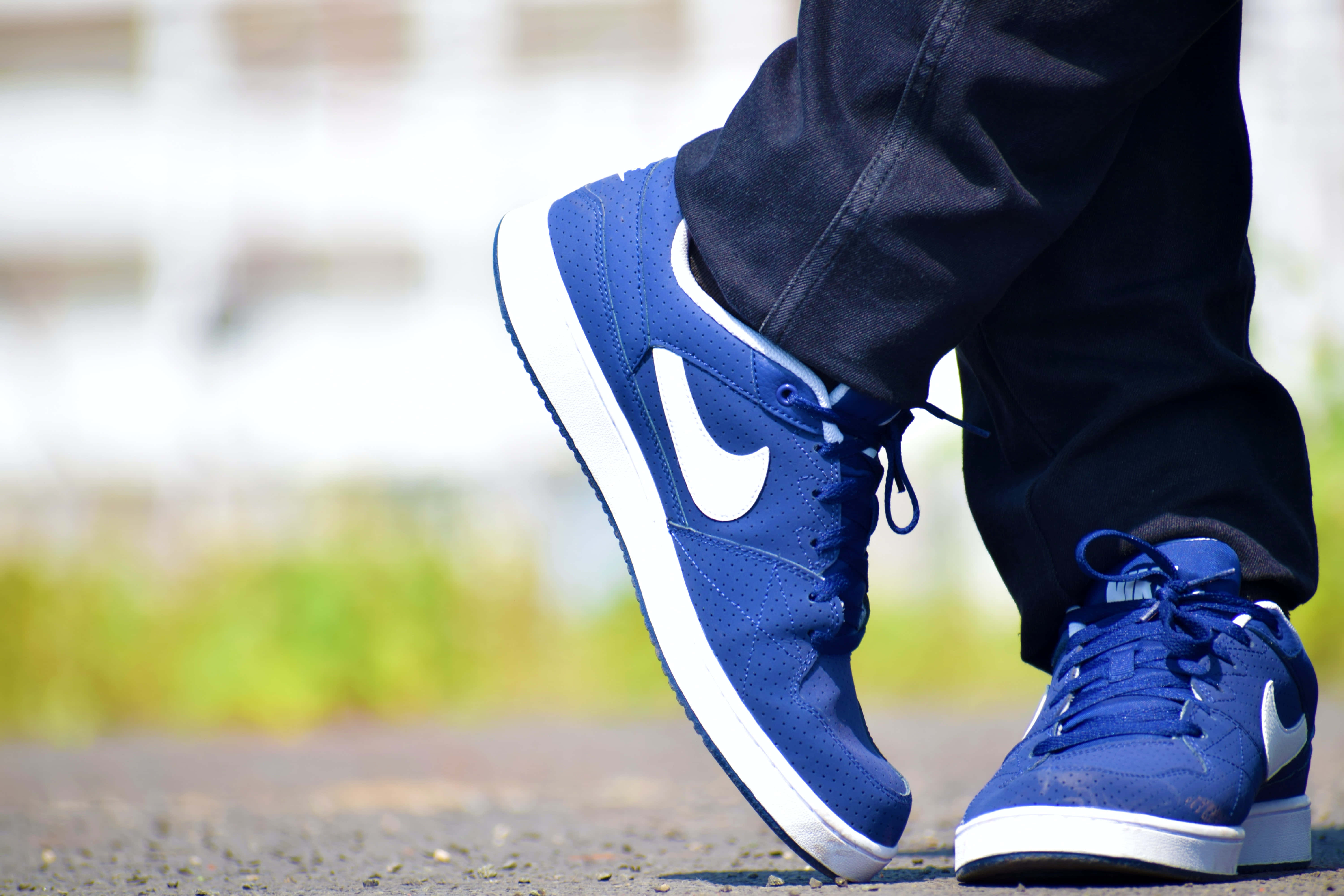 Footwear Design 桌布 壁紙 — 藍色Nike運動鞋特寫，帶白色swoosh標誌，搭配深色牛仔褲，在碎石路上，明亮日光下。