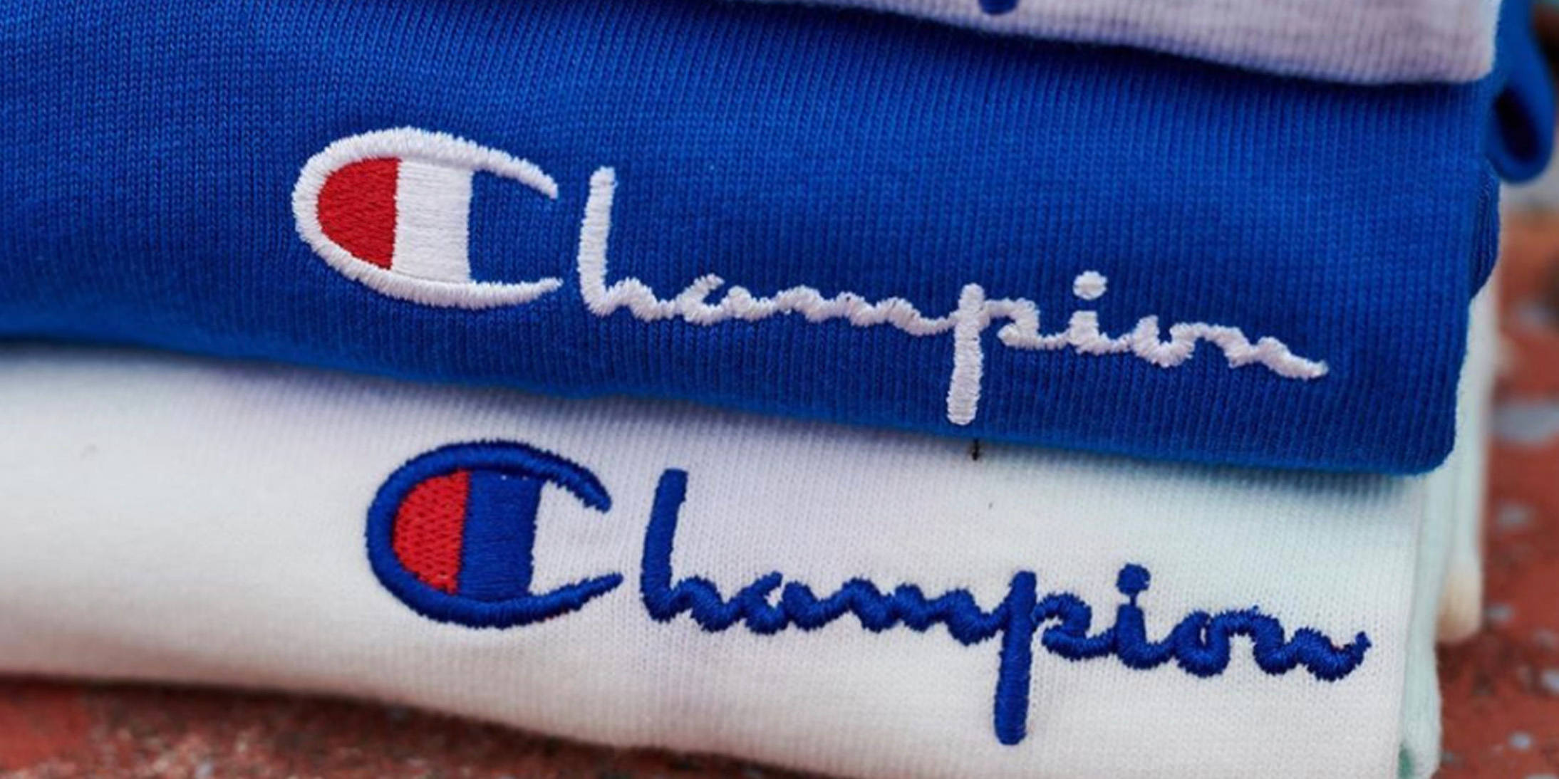 Champion 桌布 壁紙 — 藍色和白色Champion連帽衫堆疊，帶有刺繡標誌的特寫細節。