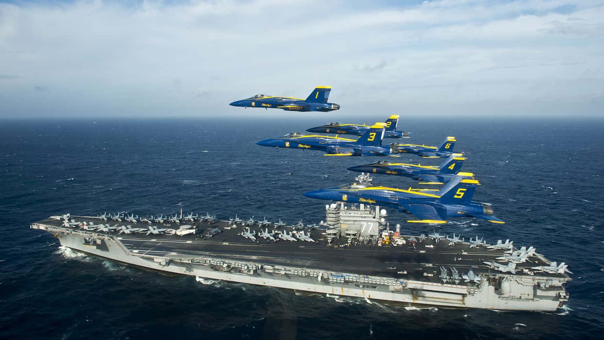 US Navy 桌布 壁紙 — 藍色和黃色的戰鬥機在公海航行的大型航空母艦上空以緊密編隊飛行。