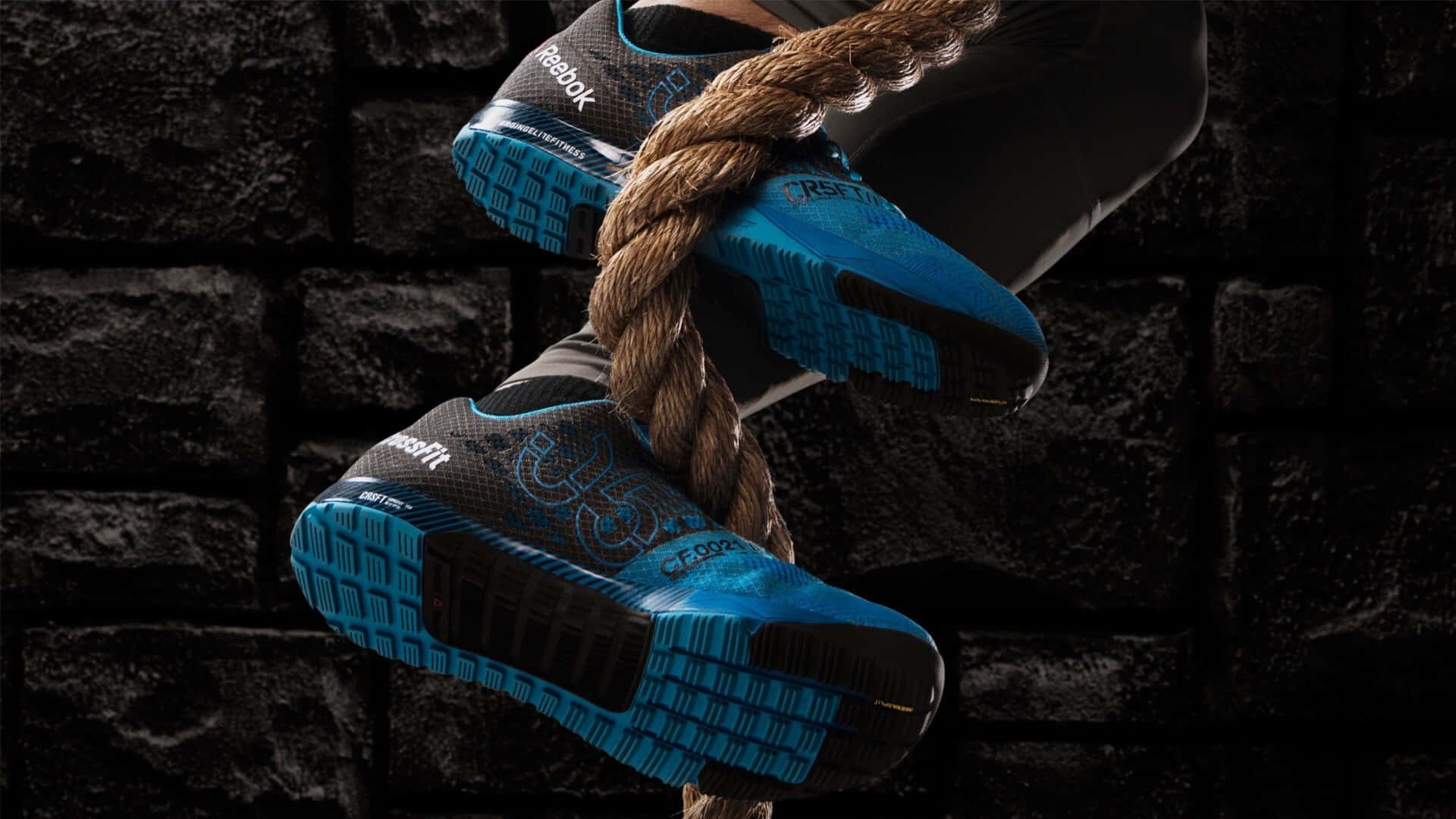 Reebok 桌布 壁紙 — 藍色和黑色Reebok越野跑鞋緊抓粗繩，靠著深色石牆的特寫。