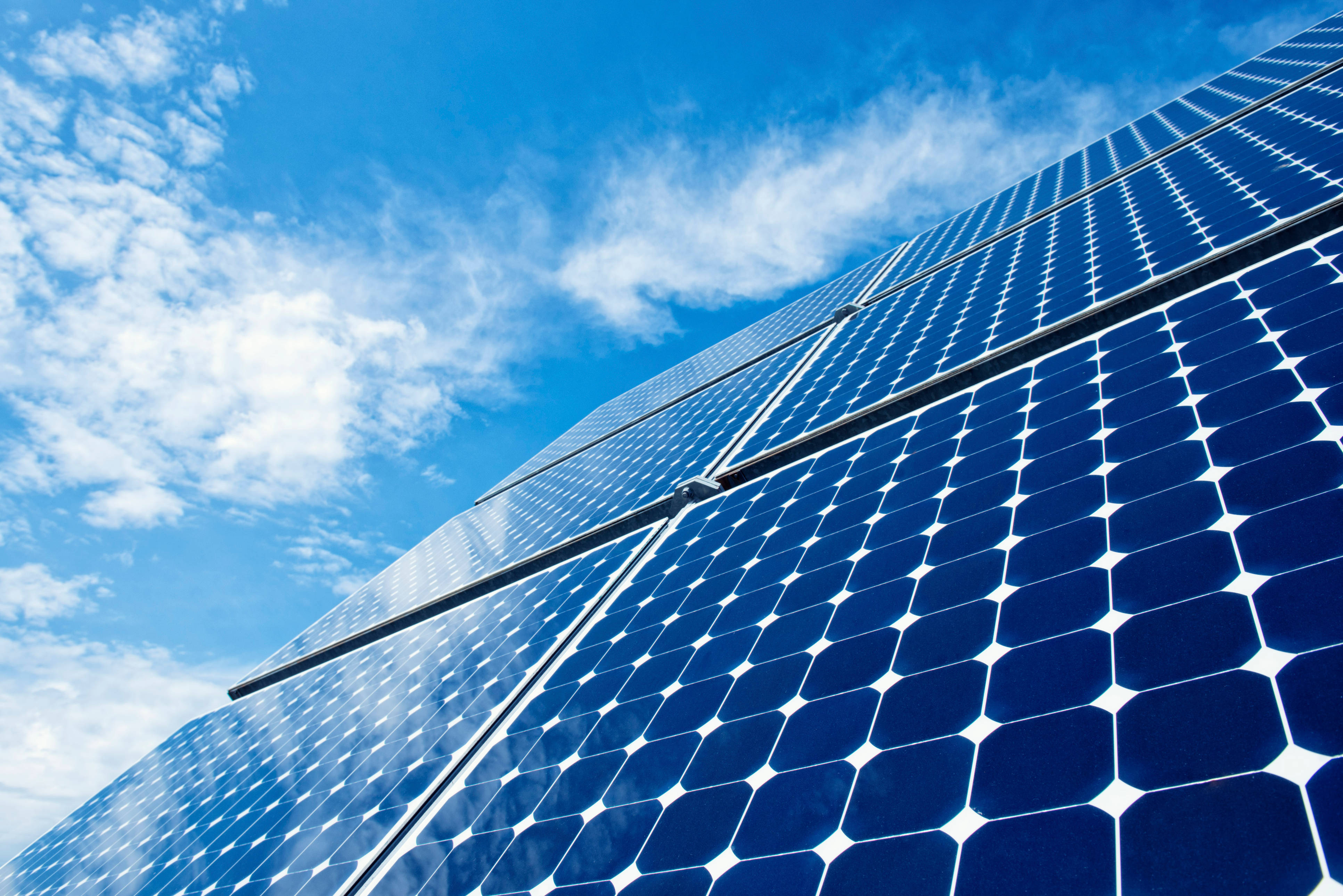Solar Panel 桌布 壁紙 — 藍色太陽能板低角度視角，反射出帶有縷縷白雲的明亮藍天。
