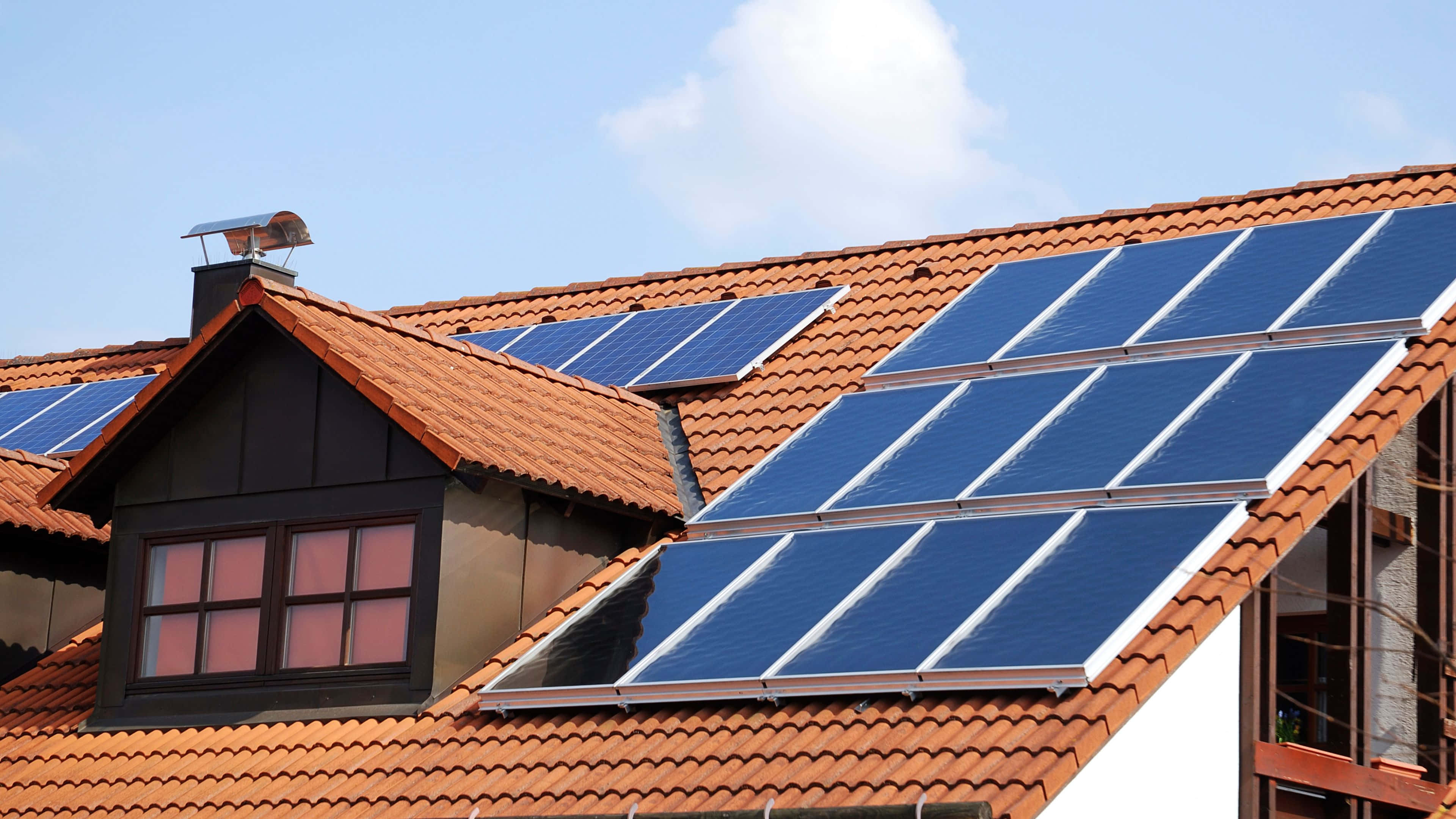 Solar Panel 桌布 壁紙 — 藍色太陽能板在明亮的藍天白雲下，在赤陶瓦屋頂上閃閃發光。