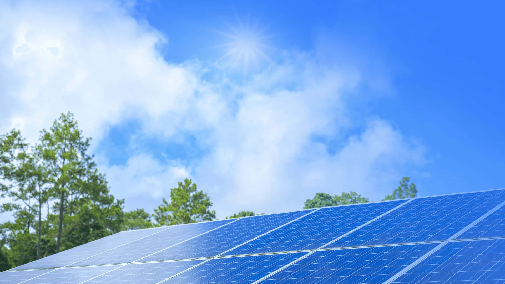 Solar Panel 桌布 壁紙 — 藍色太陽能板在明亮的陽光下閃耀，背景有蓬鬆的白雲和綠樹。