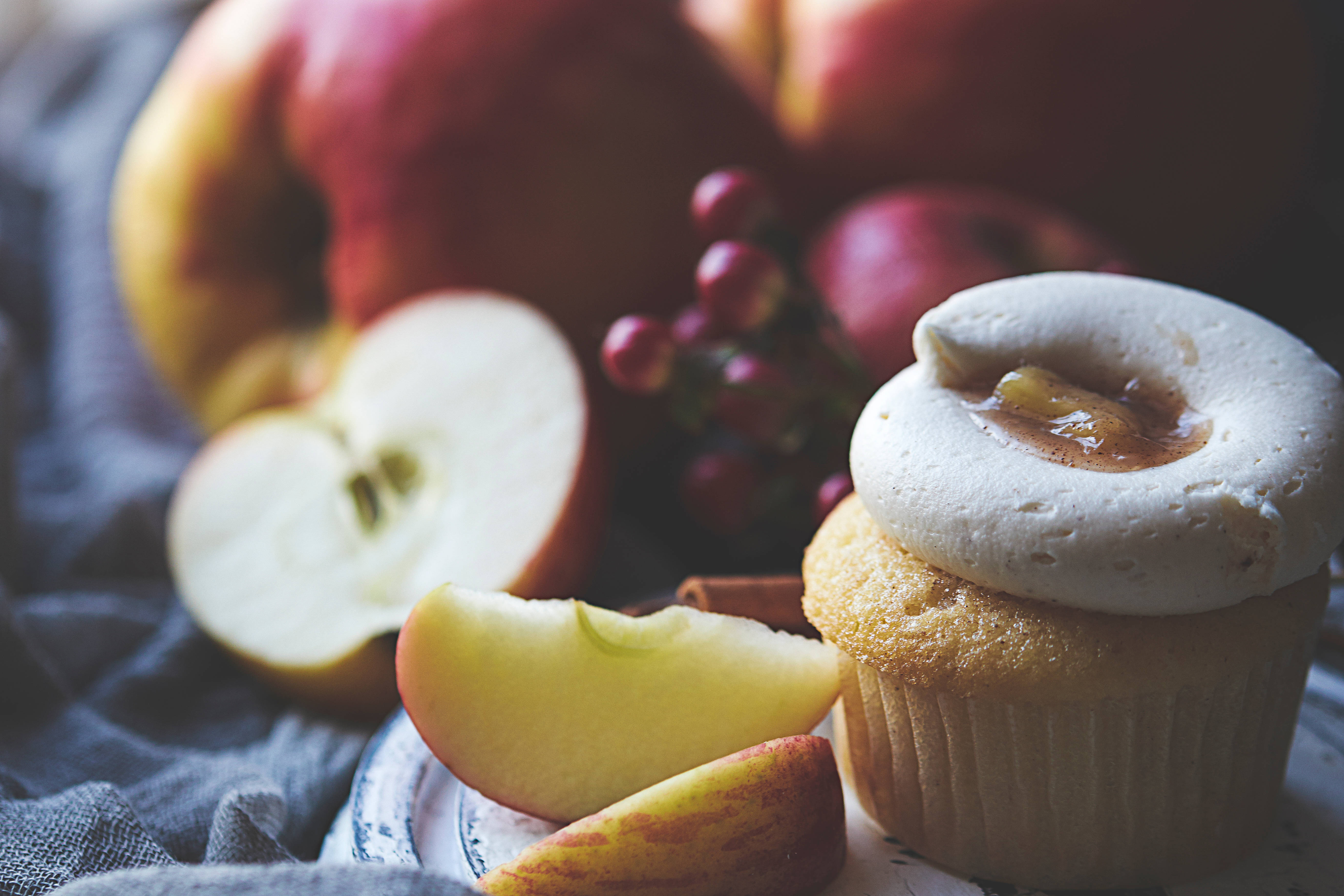 Cupcake 桌布 壁紙 — 藍色布上的紙杯蛋糕特寫，上面有白色糖霜和蘋果餡，旁邊有切片和完整的蘋果。