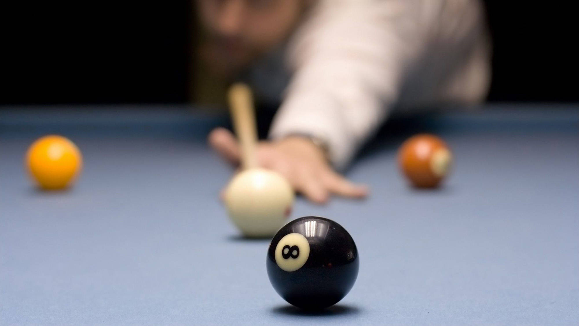 Snooker 桌布 壁紙 — 藍色撞球桌上黑色8號球的特寫，背景中球員的手和球桿模糊。