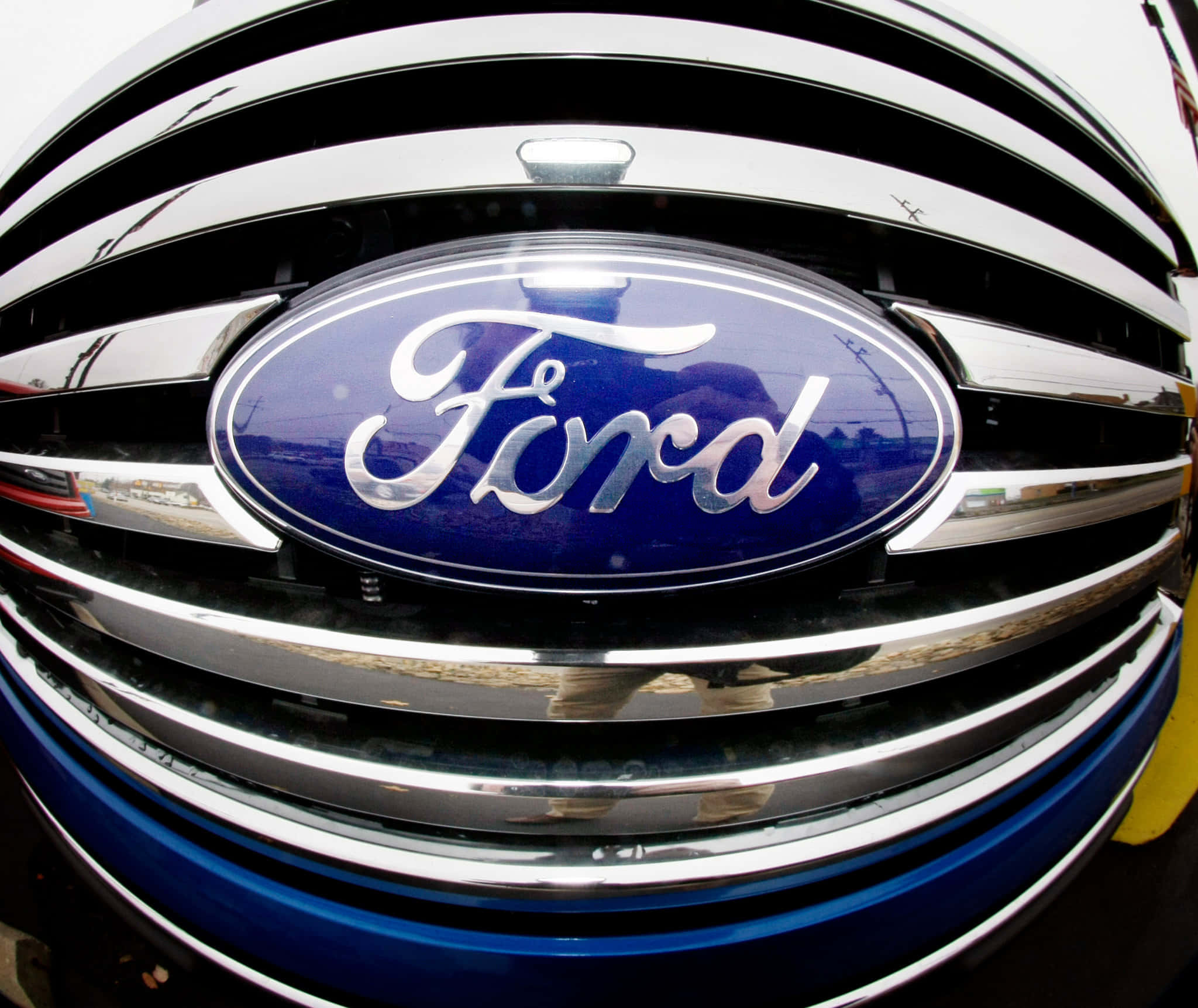 Ford Logo 桌布 壁紙 — 藍色汽車鍍鉻格柵上福特標誌的特寫，反射周圍環境。