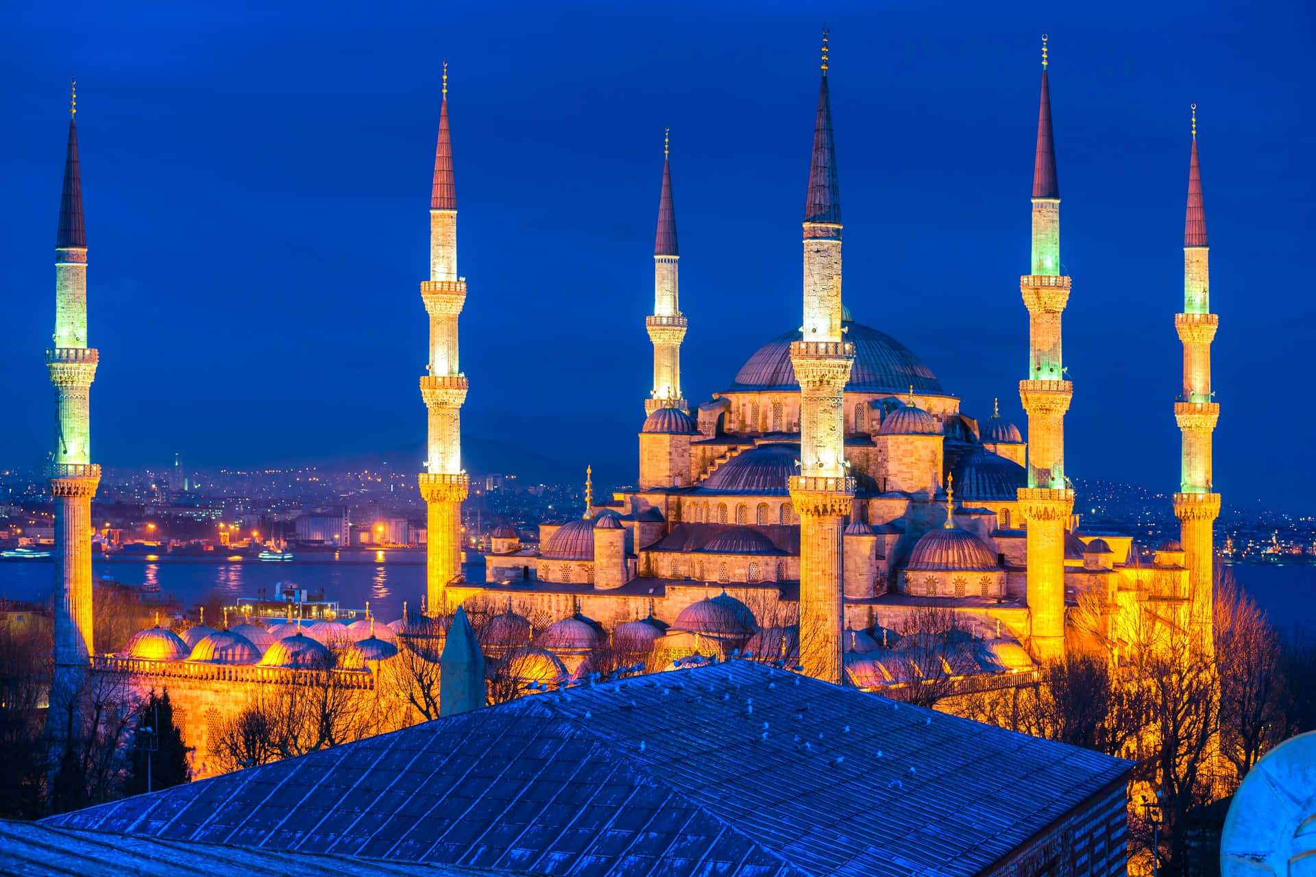 土耳其 桌布 壁紙 — 藍色清真寺在夜晚被照亮，金色宣禮塔映襯著深藍色的天空和下方的城市燈光。