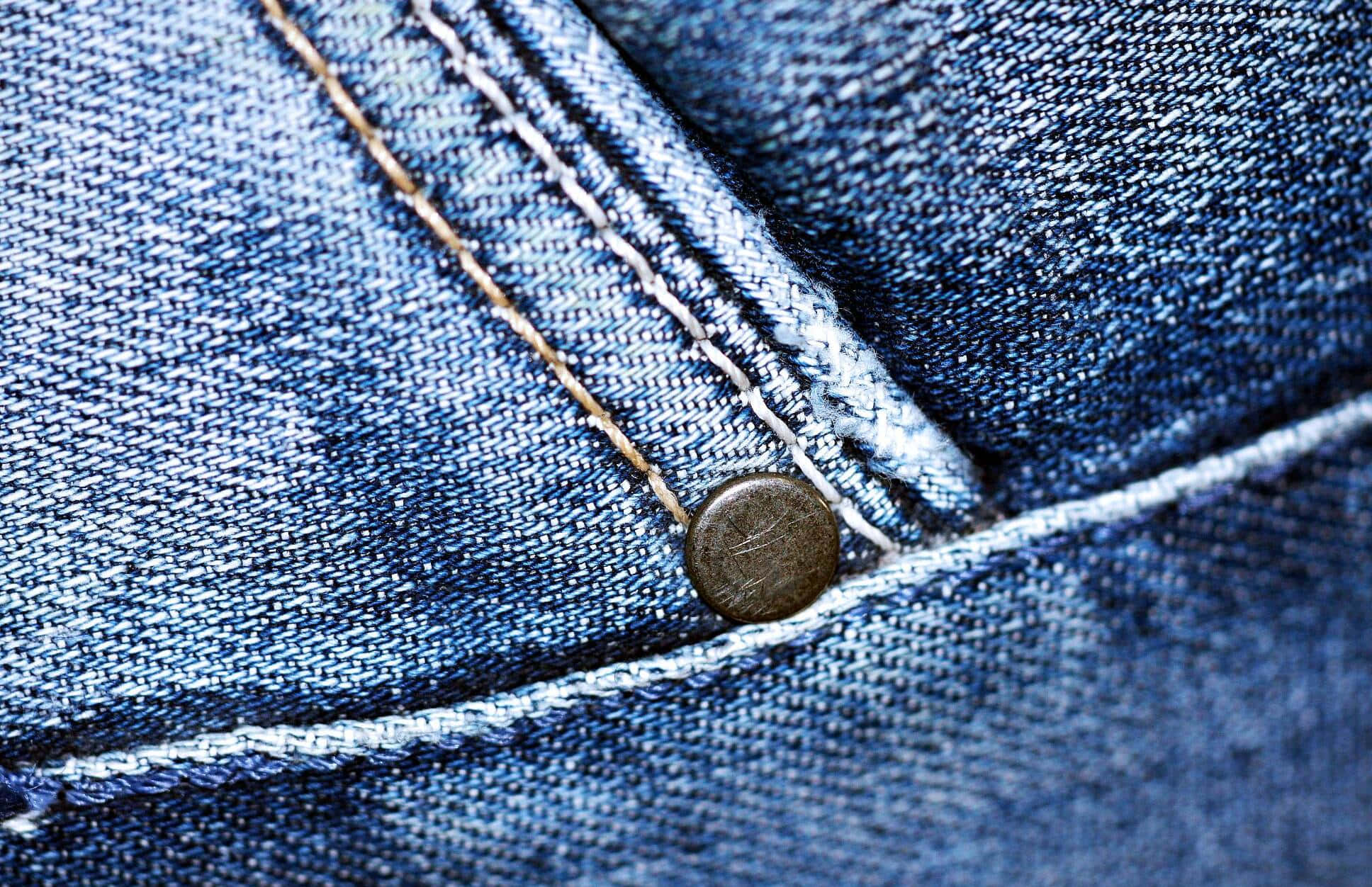 Denim 桌布 壁紙 — 藍色牛仔布料的特寫，可見縫線和金屬鈕扣，突顯質感和磨損。