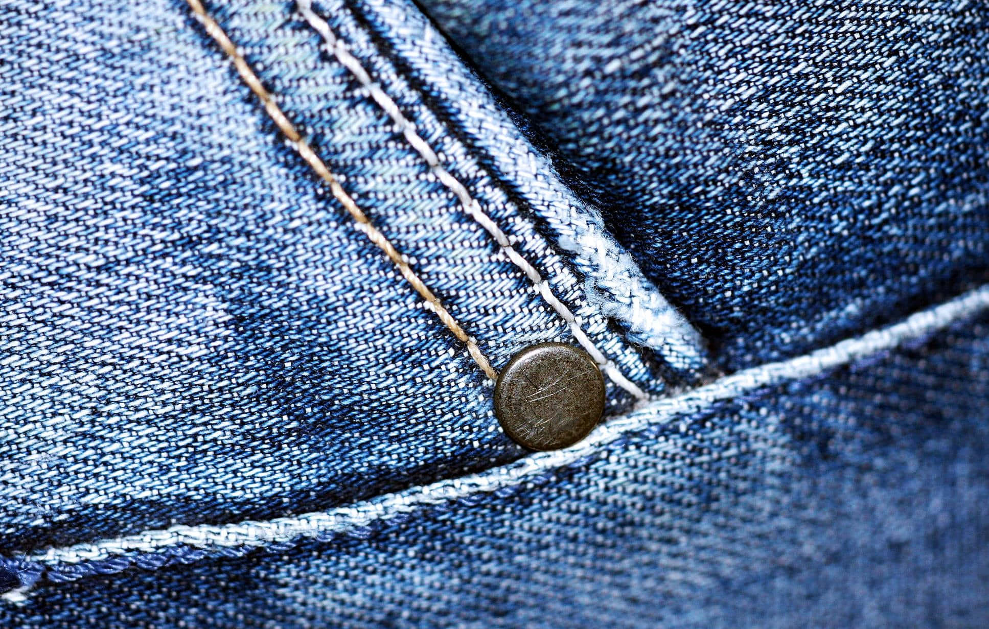 Jeans 桌布 壁紙 — 藍色牛仔布料的特寫，可見縫線和金屬鈕扣，展示質感和磨損。