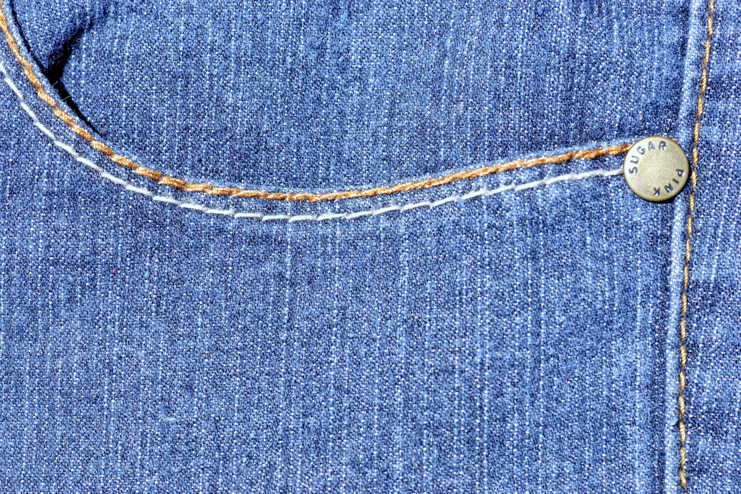 Denim 桌布 壁紙 — 藍色牛仔褲口袋特寫，帶有對比色白色和橙色縫線及品牌鈕扣。