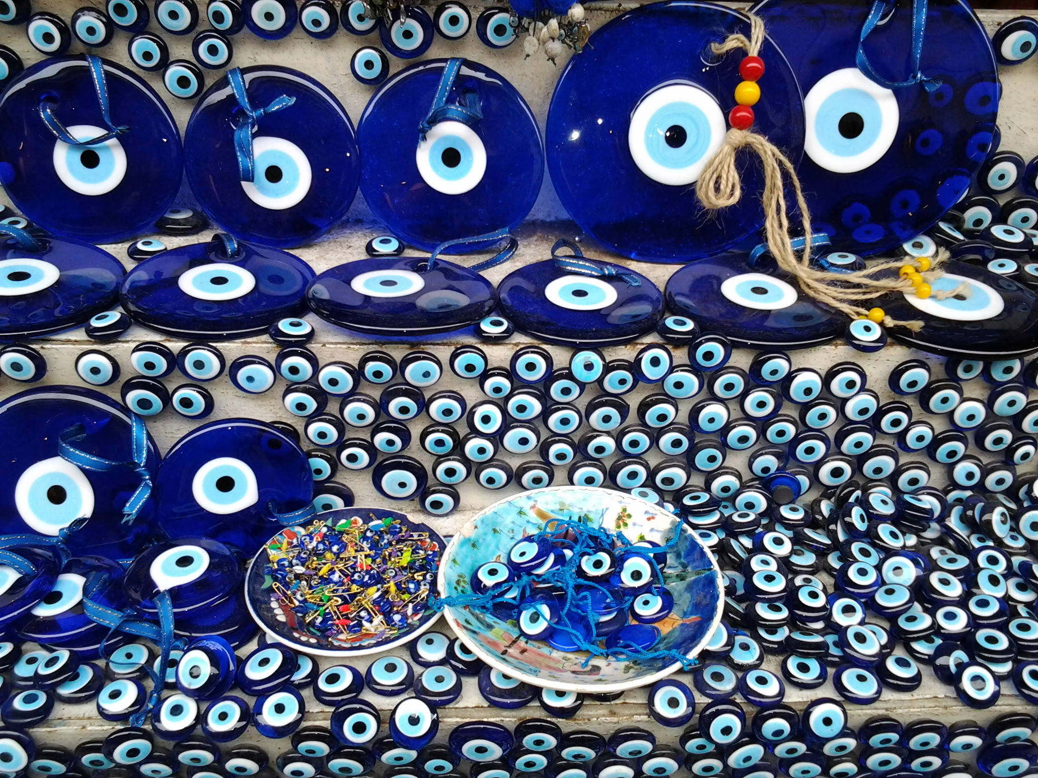 Evil Eye 桌布 壁紙 — 藍色玻璃邪眼護身符在木架上排列成行，下方有兩個盛有較小護身符的碗，展示色彩鮮豔。
