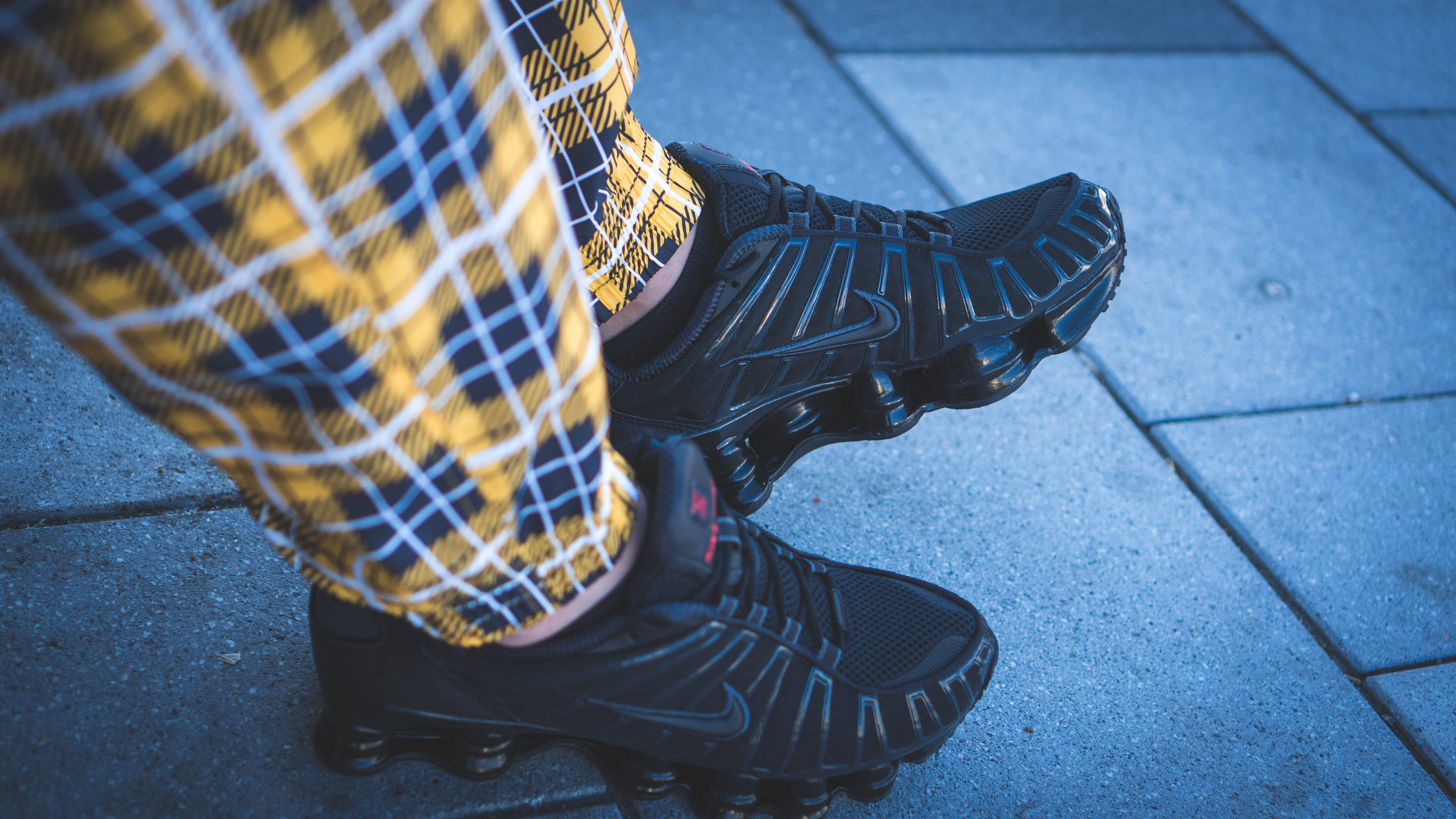 Checkered 桌布 壁紙 — 藍色瓷磚人行道上穿著黃色格紋褲的黑色Nike運動鞋特寫，可見氣墊。