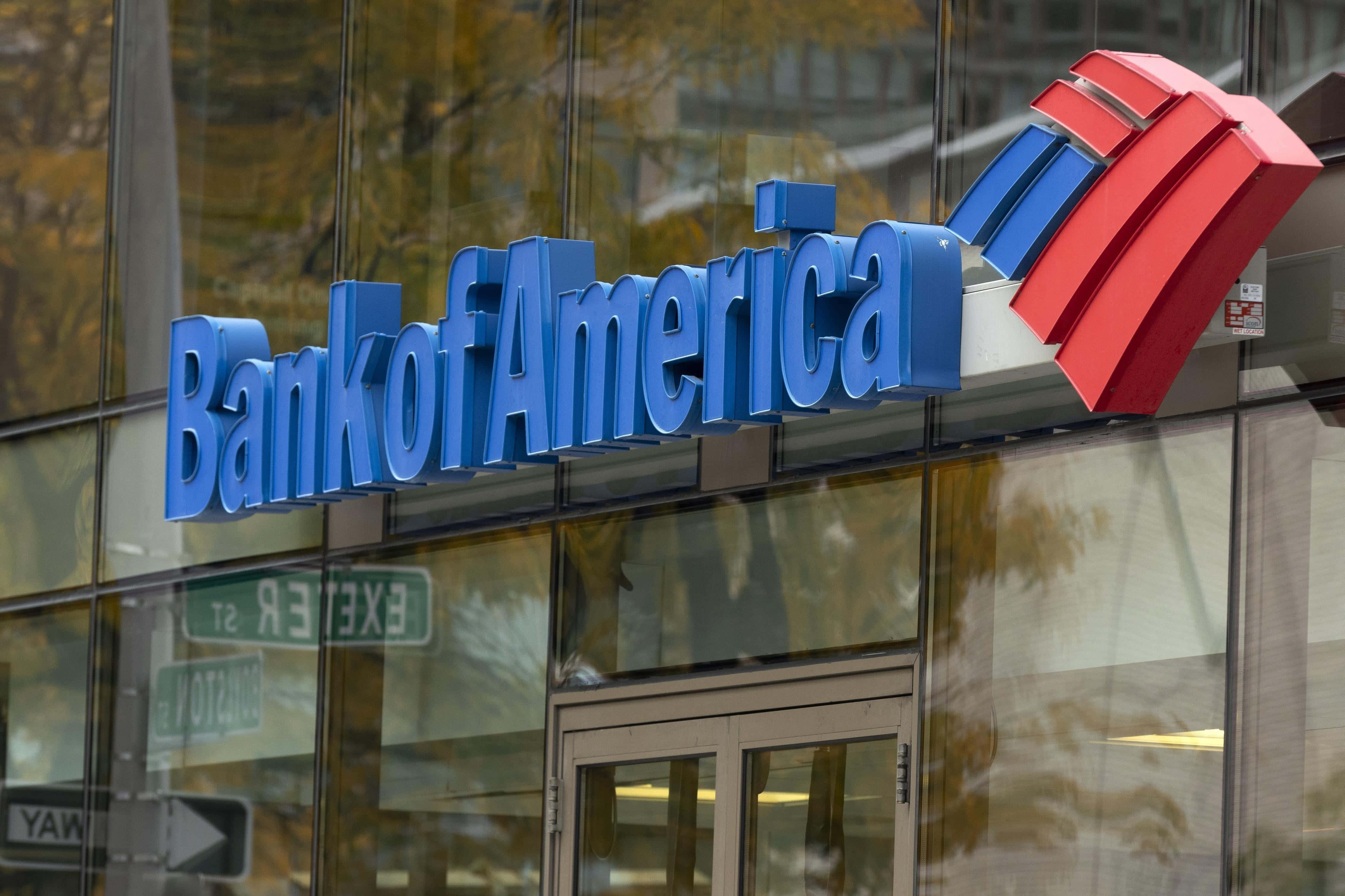 Bank Of America 桌布 壁紙 — 藍色美國銀行標誌，帶有紅色和藍色條紋，安裝在玻璃建築外牆上，反射出秋天的樹木。