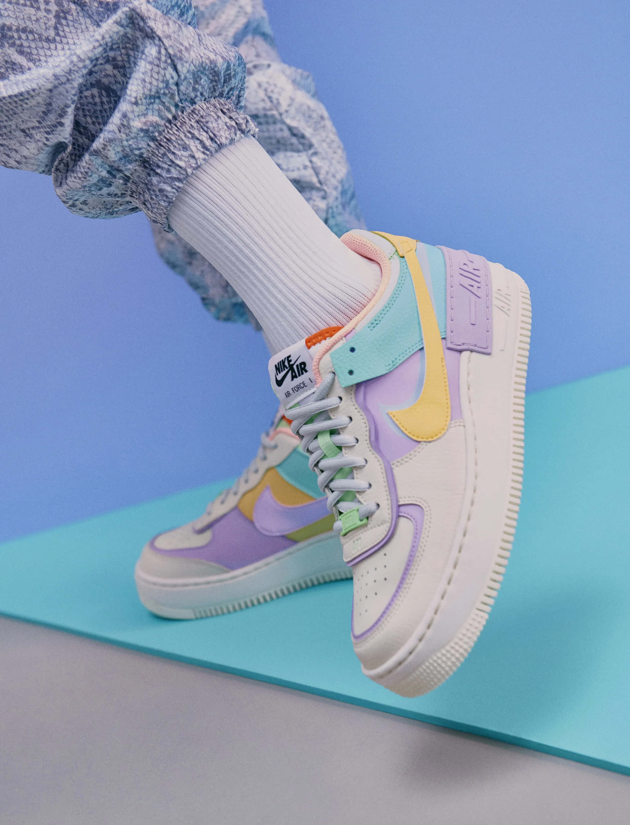 Nike 桌布 壁紙 — 藍色背景上，柔和色調的Nike Air Force 1運動鞋配上相配的襪子和圖案褲子的特寫。
