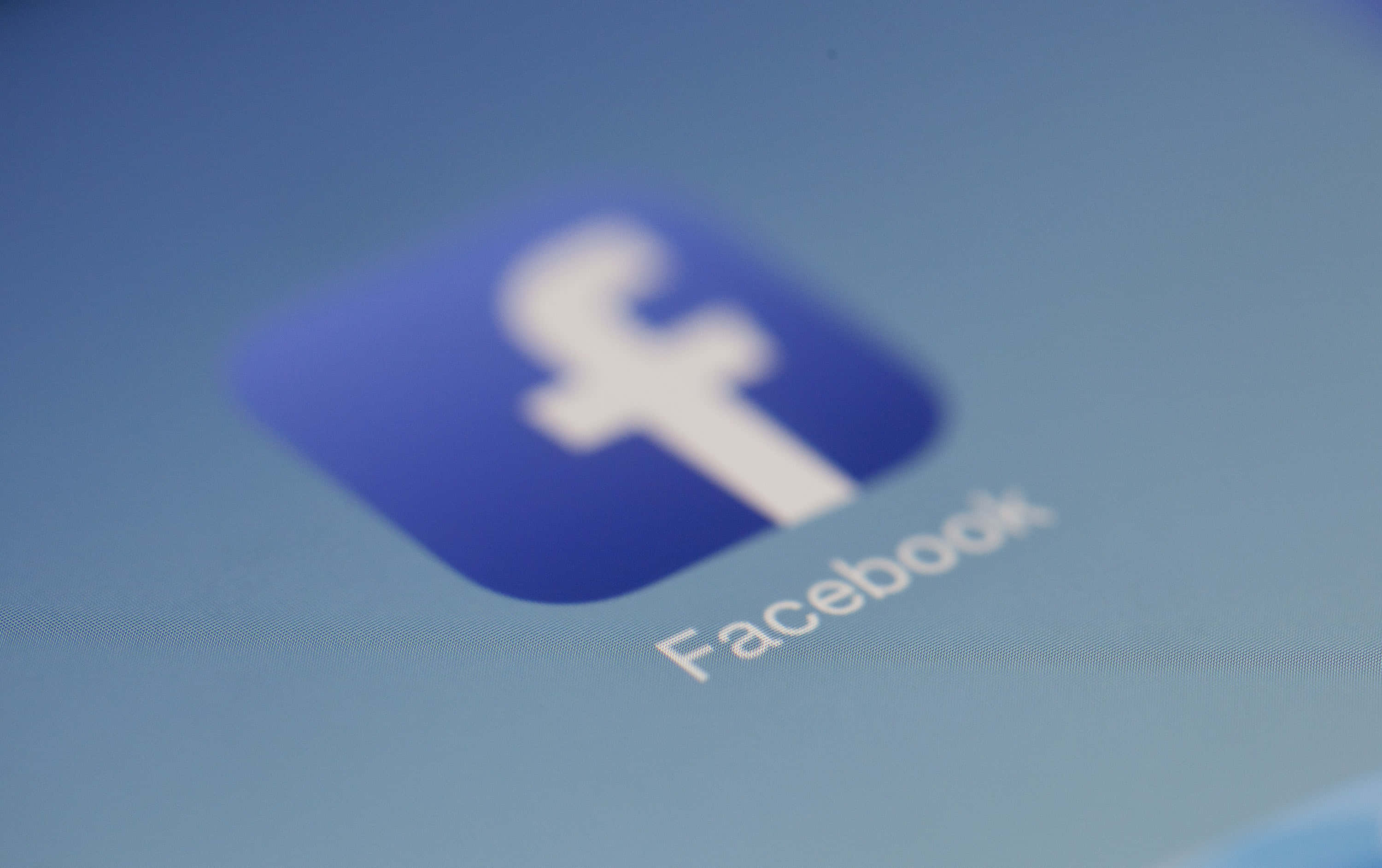 Facebook 桌布 壁紙 — 藍色螢幕上略為模糊的 Facebook 應用程式圖示近距離特寫，可見像素網格。
