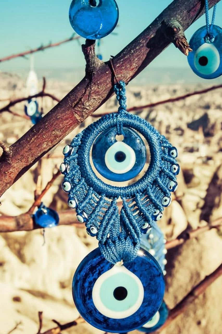 Evil Eye 桌布 壁紙 — 藍色邪眼護身符以複雜的繩結編織工藝懸掛在陽光照射的樹枝上，背景是岩石沙漠。