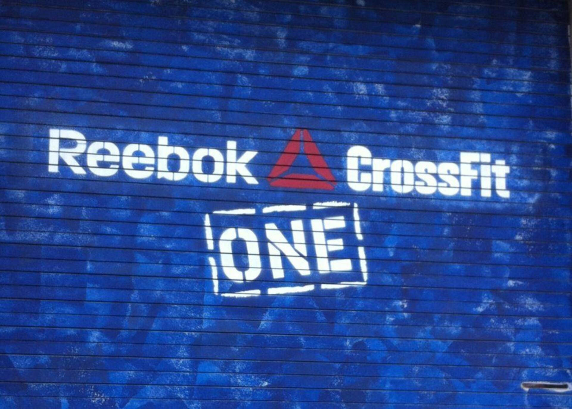 Reebok 桌布 壁紙 — 藍色金屬百葉窗上顯示一個大膽的白色和紅色Reebok CrossFit ONE標誌，表面有紋理。