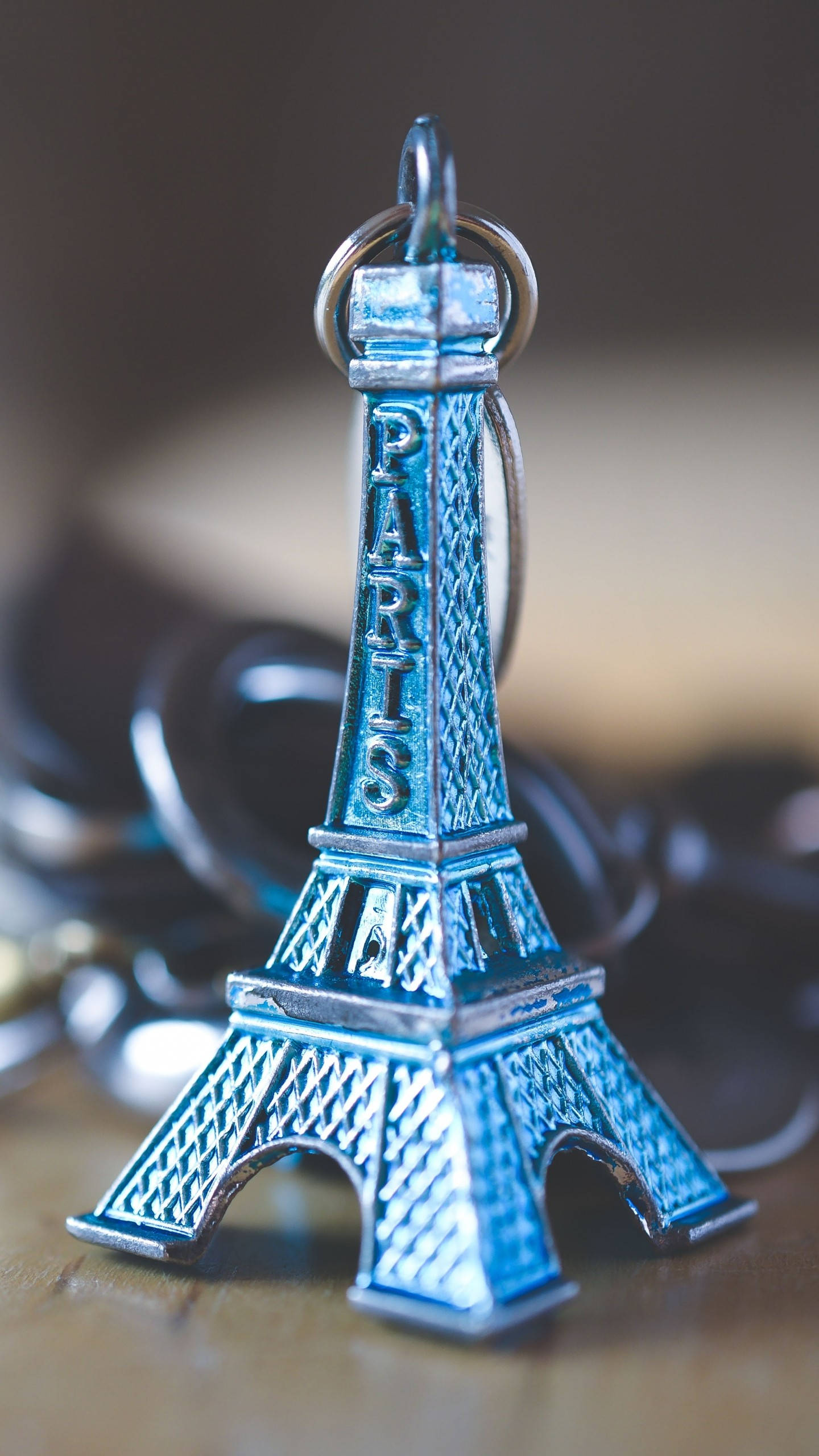 Eiffel Tower 桌布 壁紙 — 藍色金屬質感艾菲爾鐵塔鑰匙圈的特寫，放置在木質表面上，背景有模糊的鑰匙。