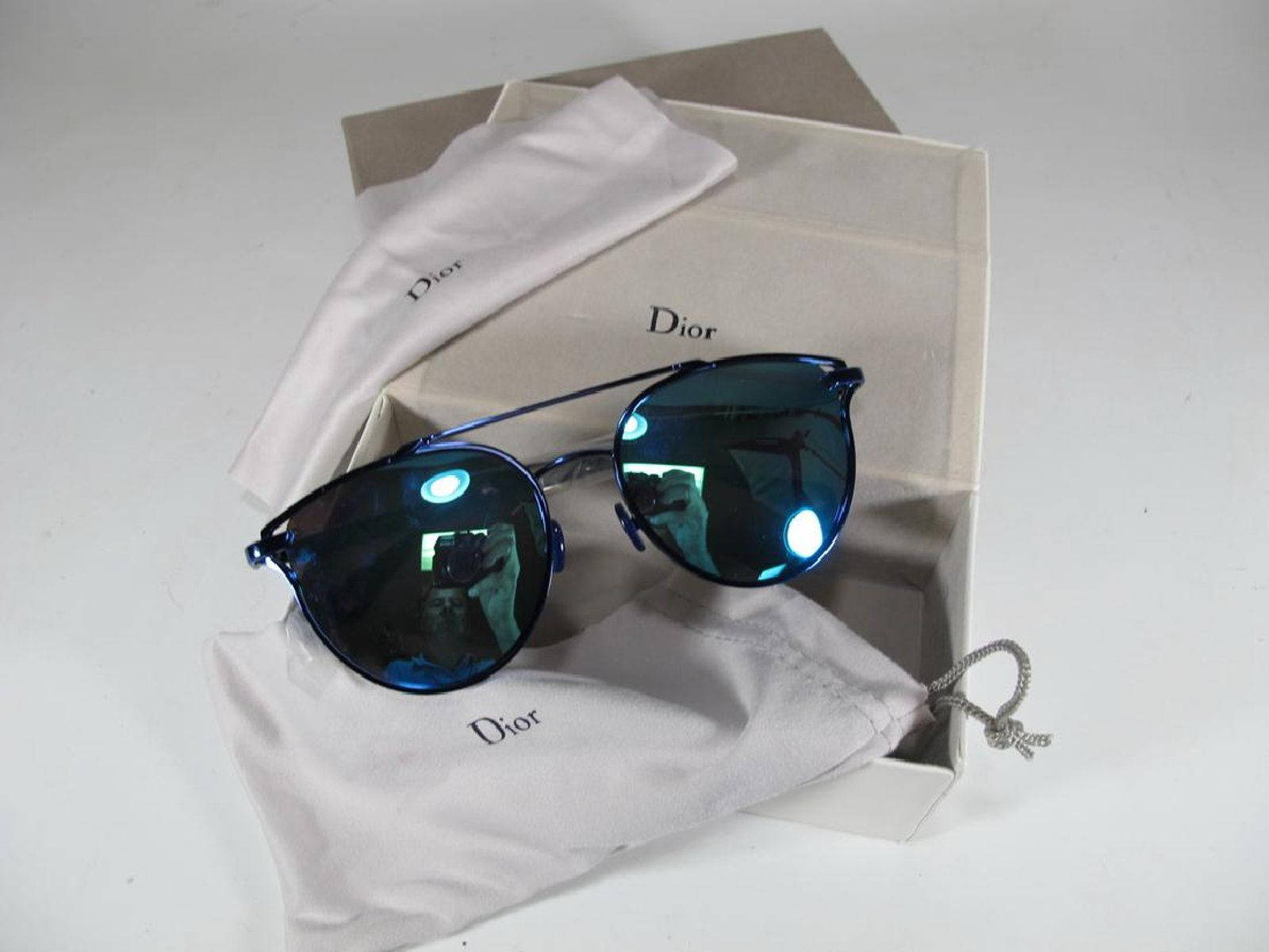 藍色鏡面Dior太陽眼鏡連品牌布料及盒子在白色表面上。 — Dior 動態 壁紙
