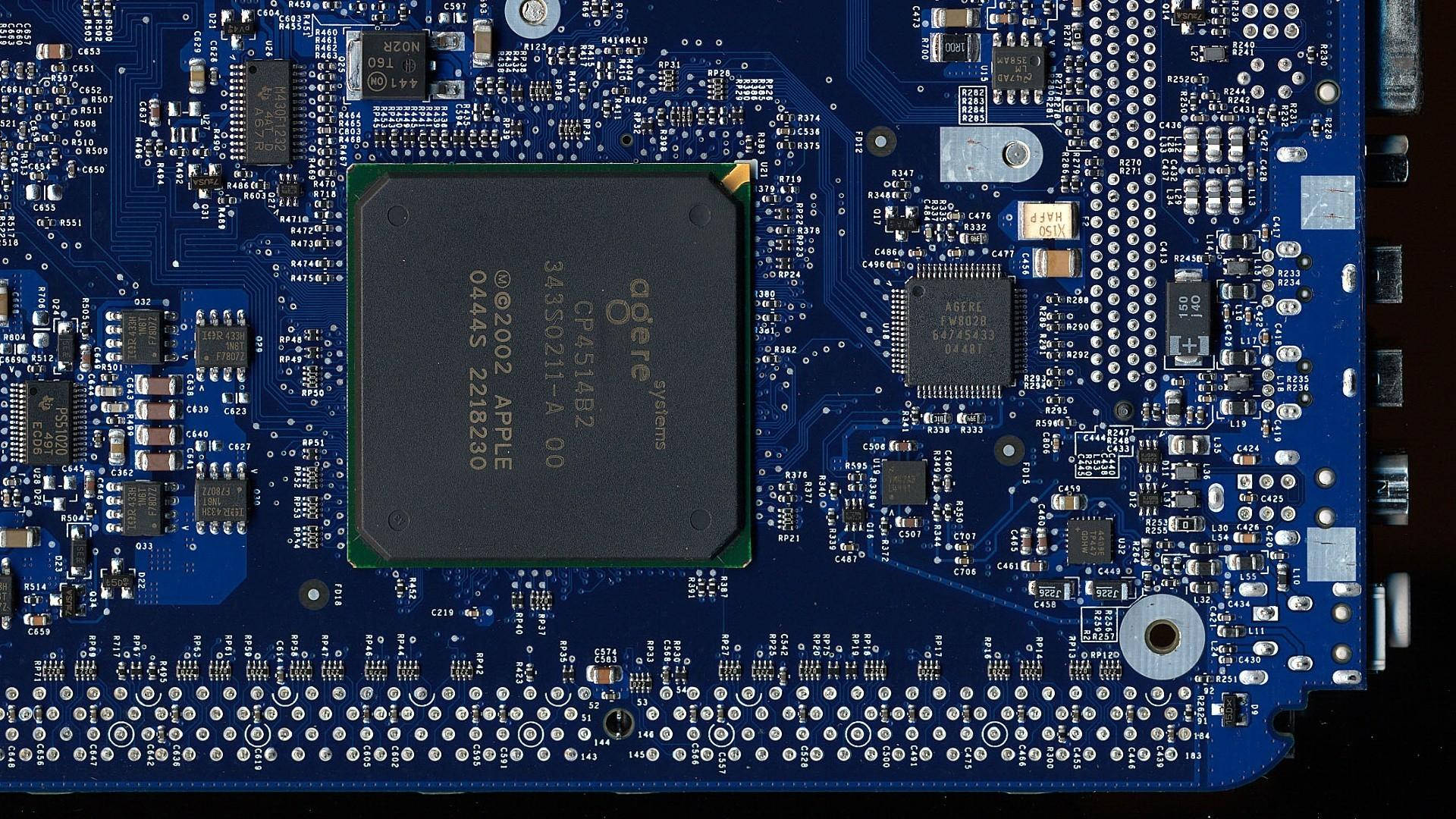 Circuit 桌布 壁紙 — 藍色電路板的特寫，中央有一個 Apple CPU 晶片，周圍是複雜的電子元件。