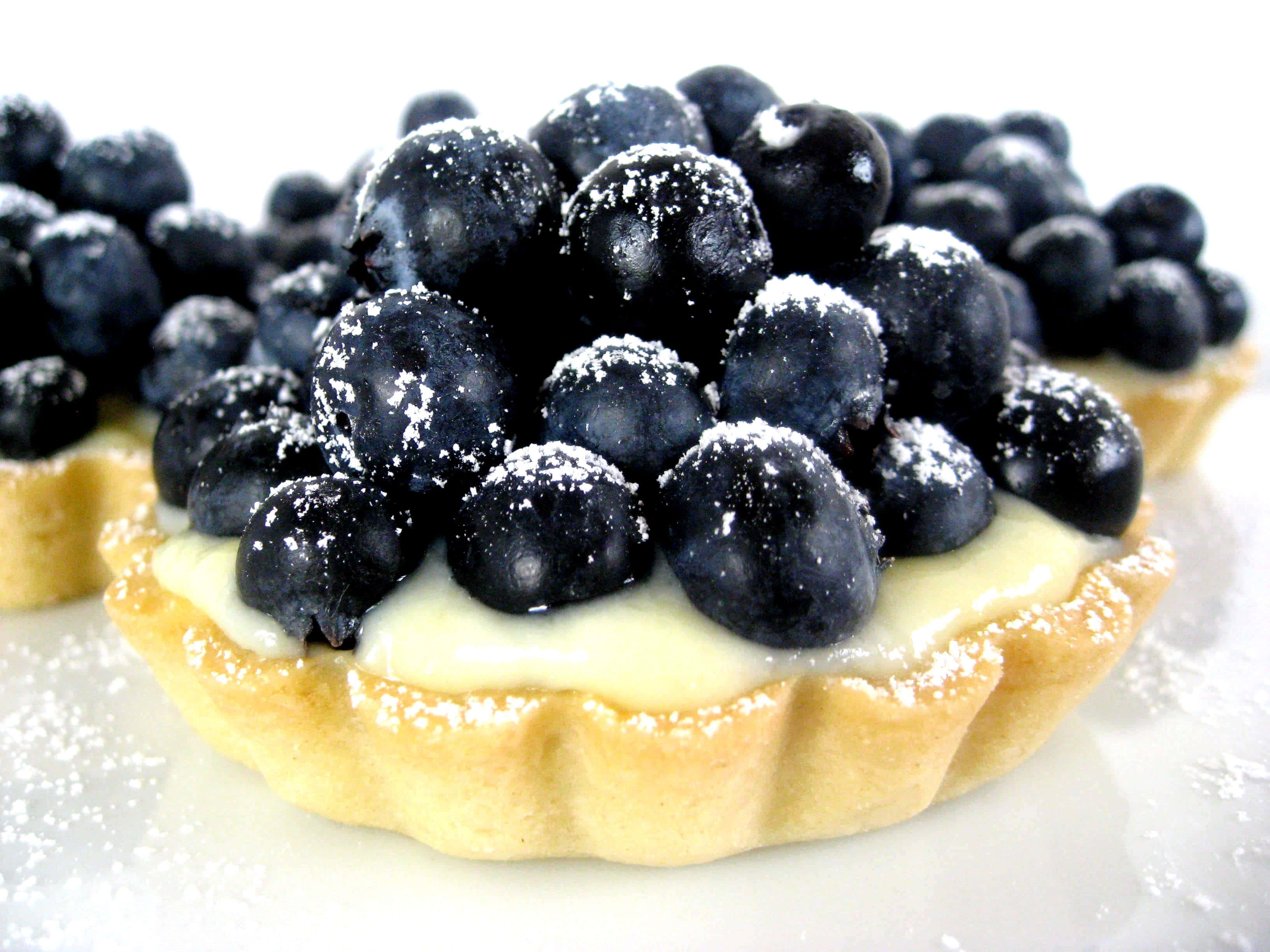 Blueberries Tart 桌布 壁紙 — 藍莓塔撒上糖粉，置於白色表面上的特寫。
