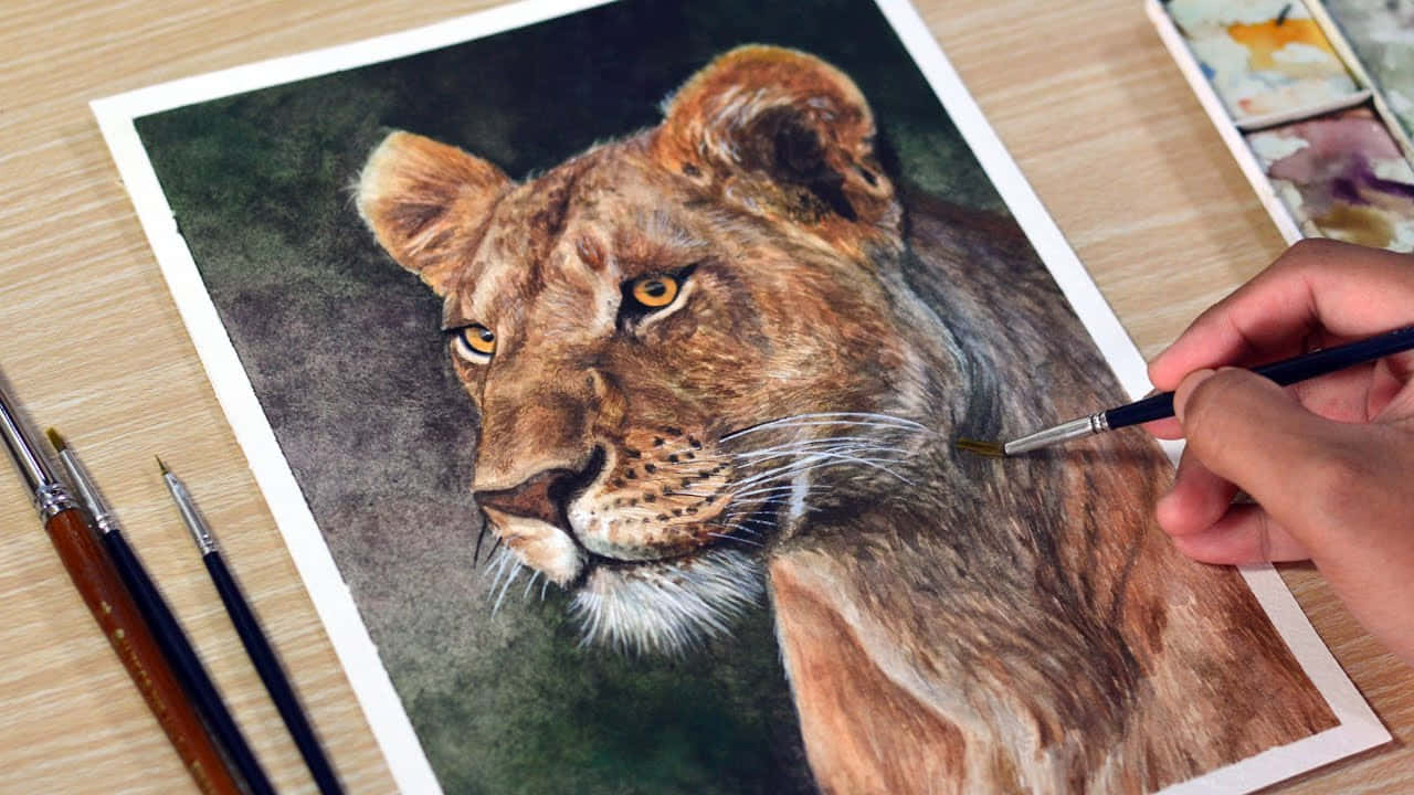 Lion Head 桌布 壁紙 — 藝術家的手正在紙上仔細繪製一幅詳細的母獅水彩肖像，畫筆和調色板就在附近。