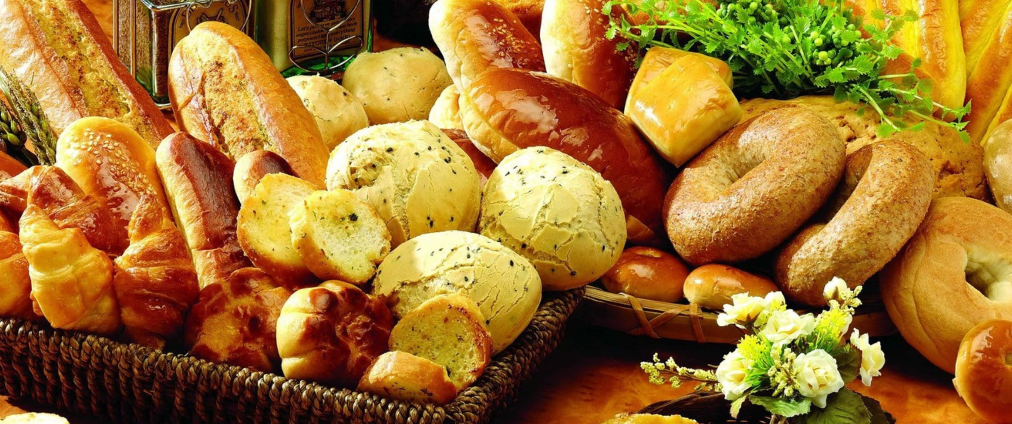 3440x1440p Pastries 桌布 壁紙 — 藤籃中盛載著各式各樣金黃色的手工麵包和糕點，並以新鮮香草和精緻的白花點綴。