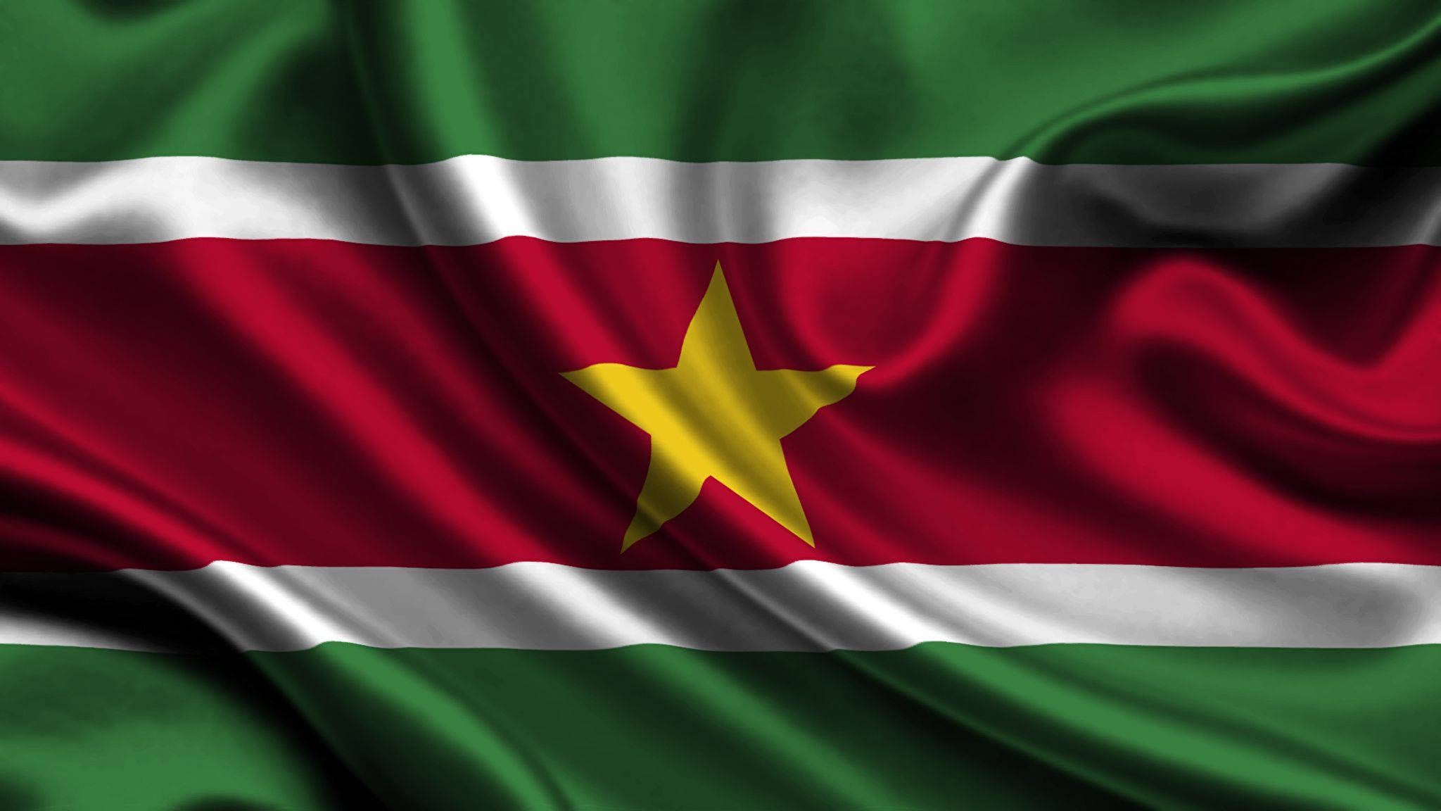 Suriname 桌布 壁紙 — 蘇利南國旗飄揚的近距離特寫，帶有濃郁的綠色、紅色和白色條紋，紅色帶中央有一顆金色星星。