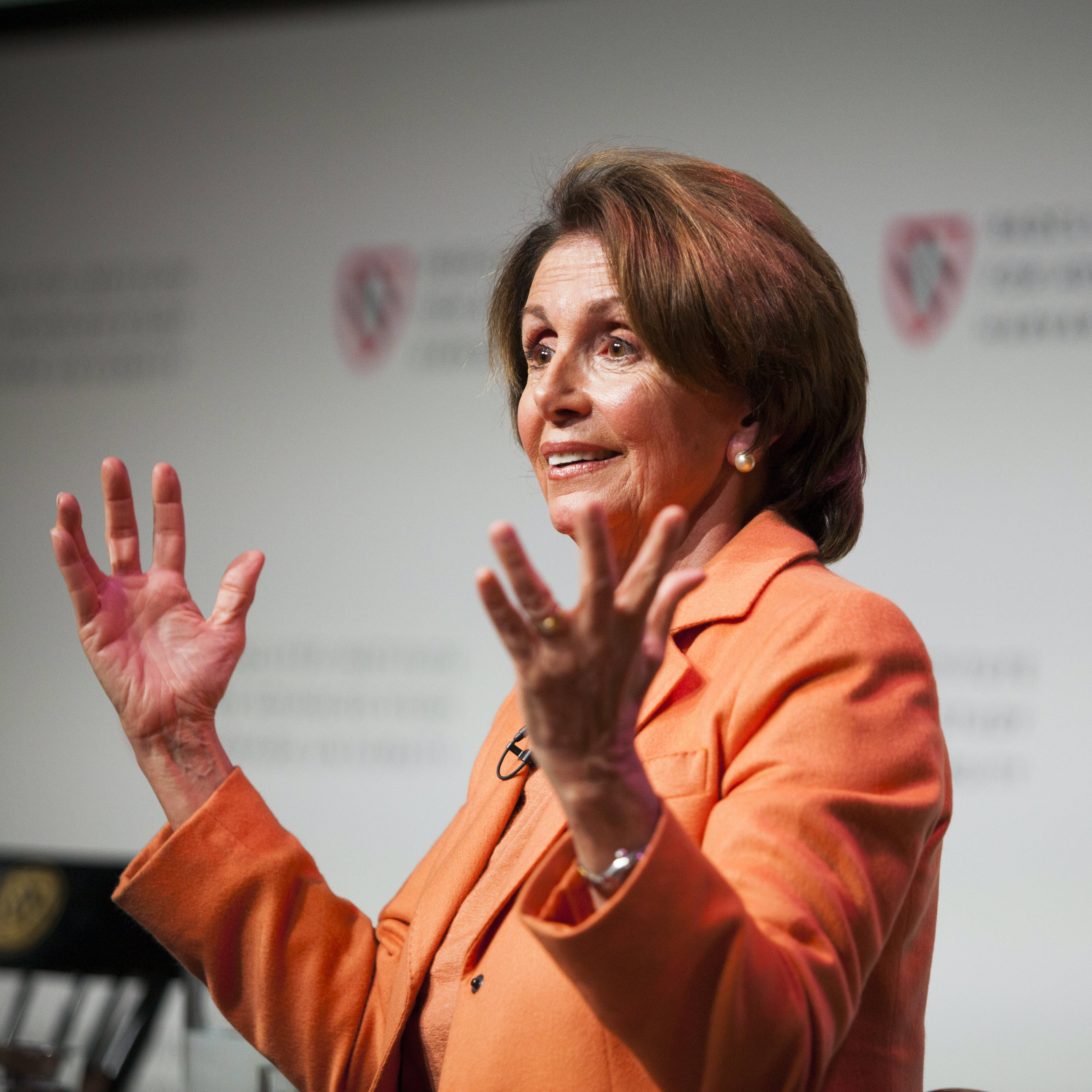 Nancy Pelosi 桌布 壁紙 — 蘭西·裴洛西穿著橙色西裝外套在正式活動中熱情地做手勢說話。