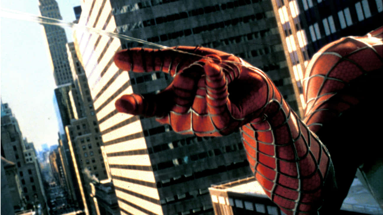Spider-man Web Shooter 桌布 壁紙 — 蜘蛛人戴著手套的手向陽光明媚、高樓林立的城市景觀射出蜘蛛網。