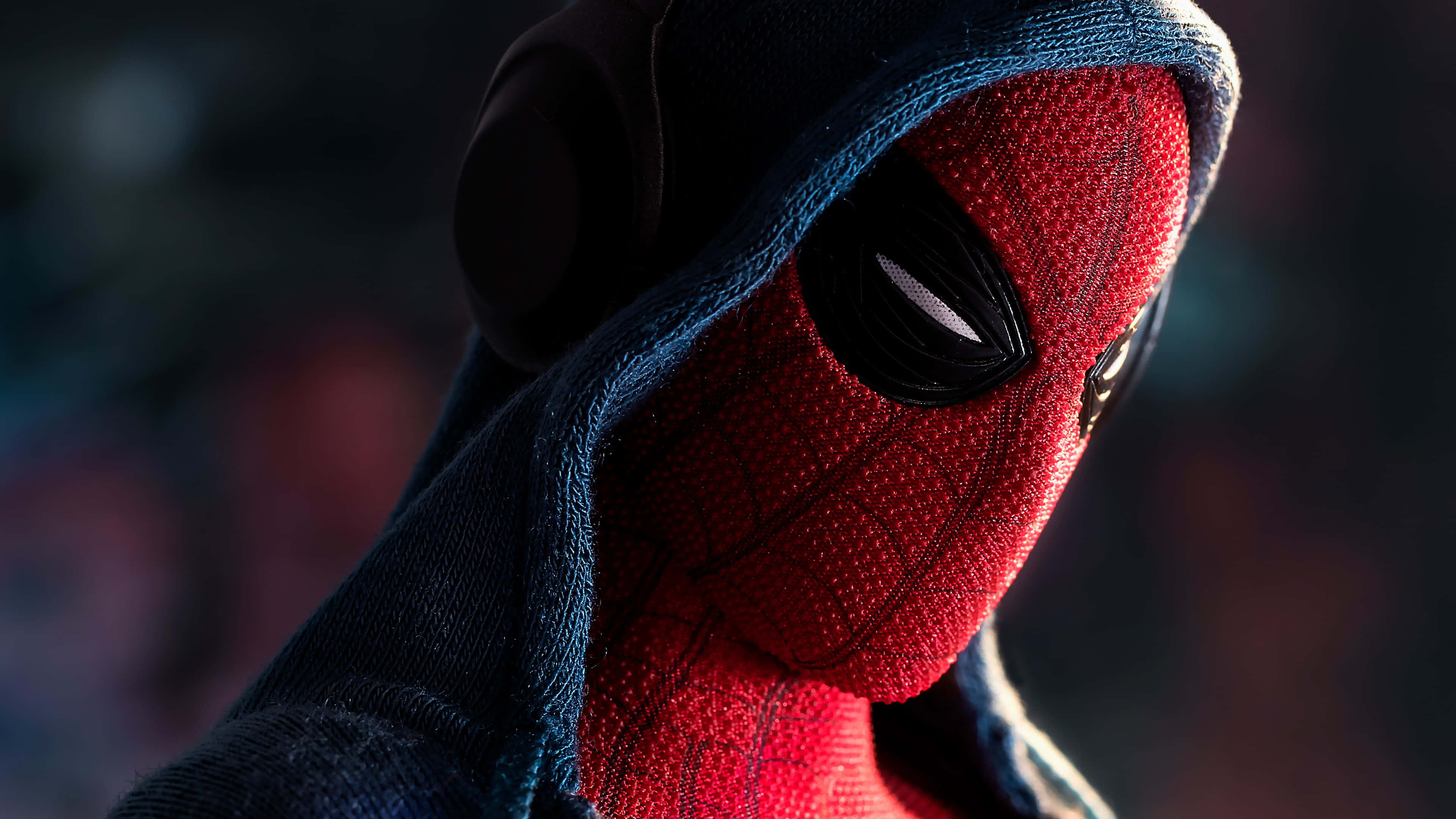 Spider Man Cool 桌布 壁紙 — 蜘蛛人穿著深色連帽衫，紅色戰衣帶有紋理，眼睛發光，背景模糊的特寫。