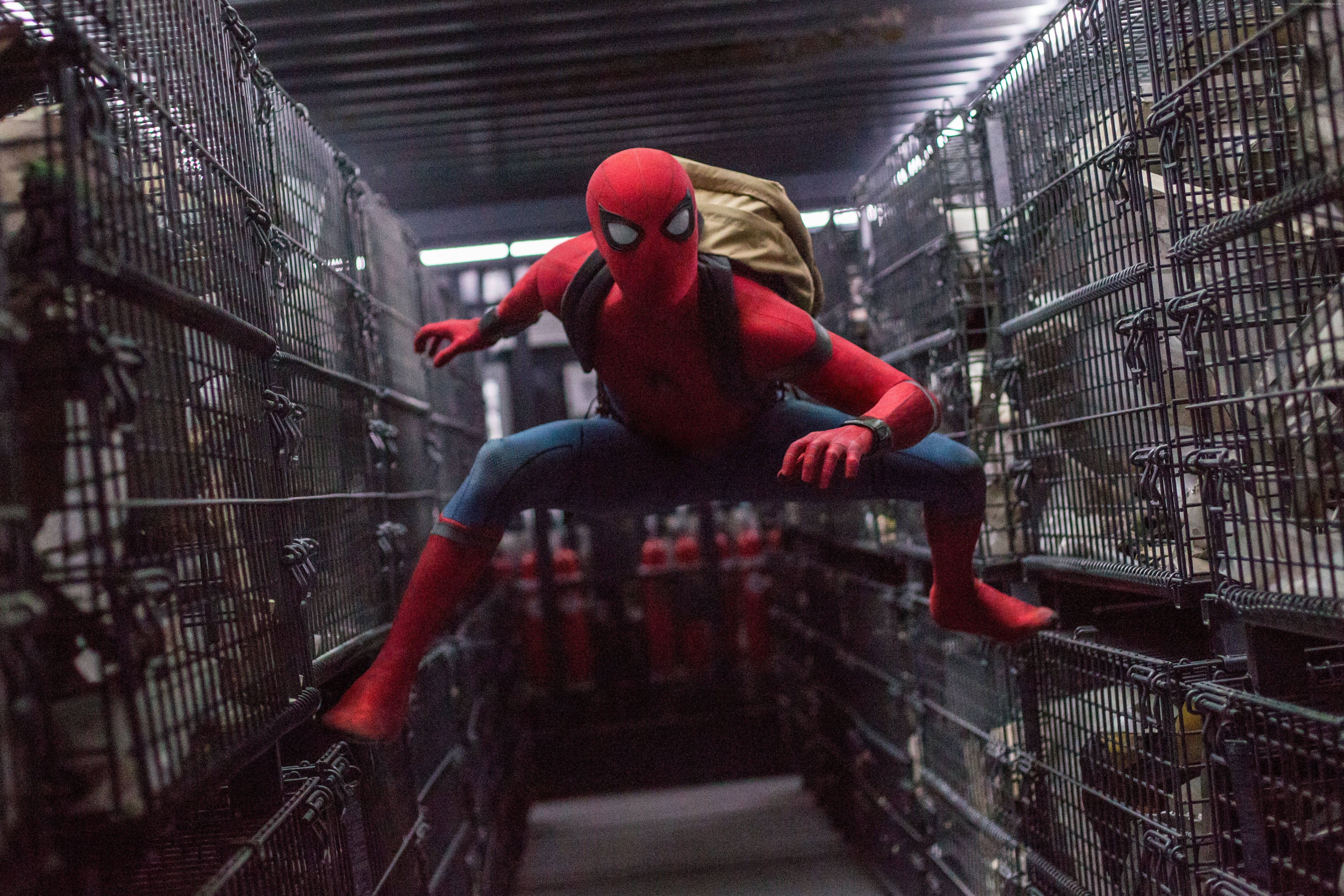 4K Marvel 壁紙 桌布 壁紙 — 蜘蛛人穿著紅色戰衣，在昏暗的工業倉庫中跳躍於金屬籠子之間。