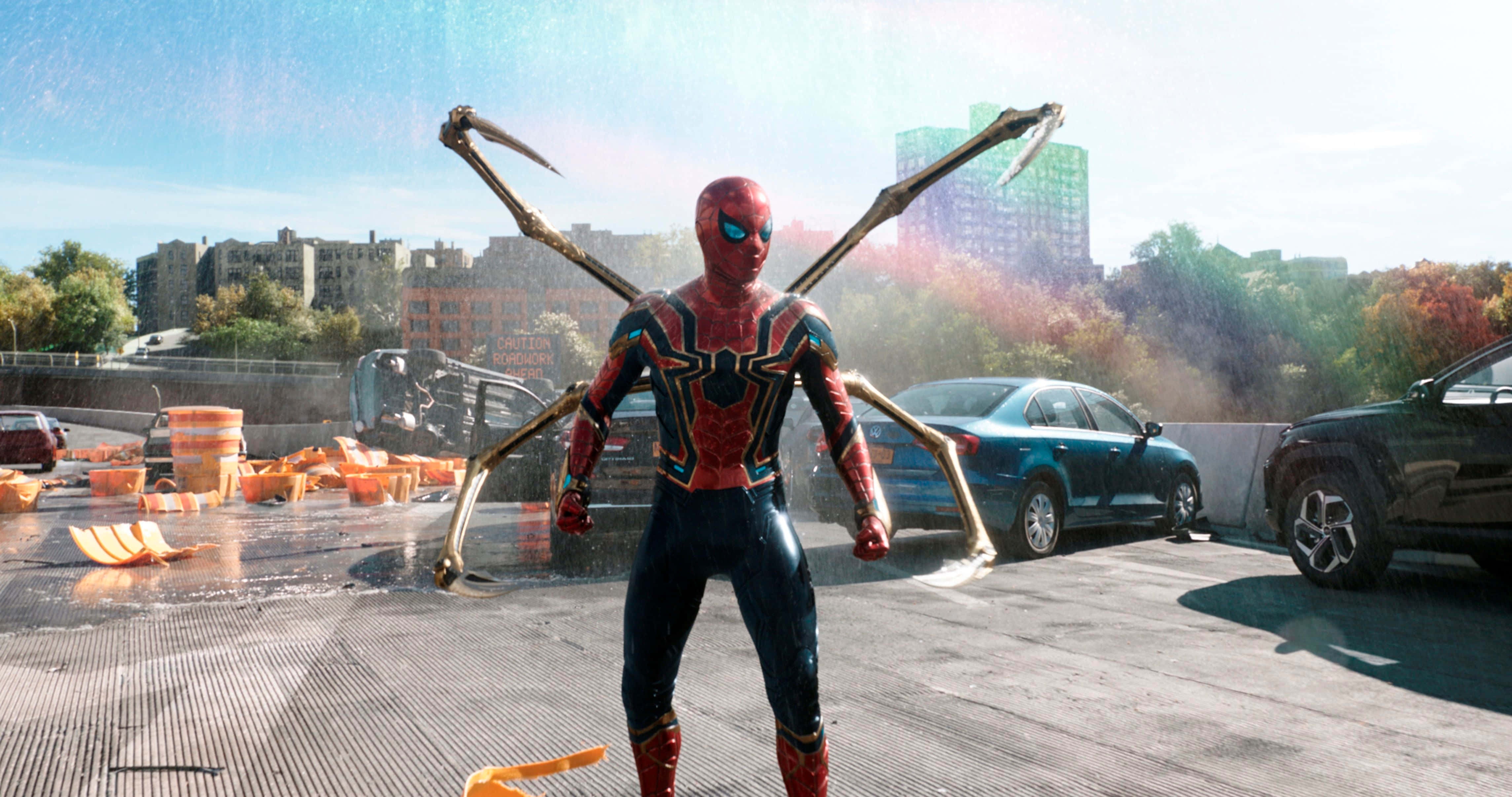 Spider Man No Way Home 桌布 壁紙 — 蜘蛛人穿著紅金色戰衣，站在濕漉漉的屋頂上，四條機械臂在燦爛陽光下伸展開來，映襯著城市天際線。