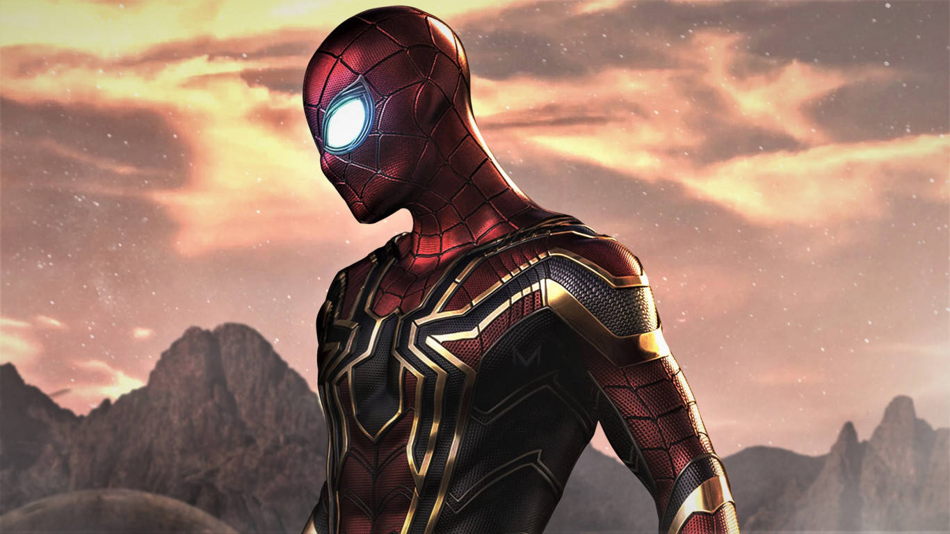 Spiderman 1366x768 桌布 壁紙 — 蜘蛛人穿著紅金色裝甲服，英勇地站在戲劇性的山脈日落天空前。