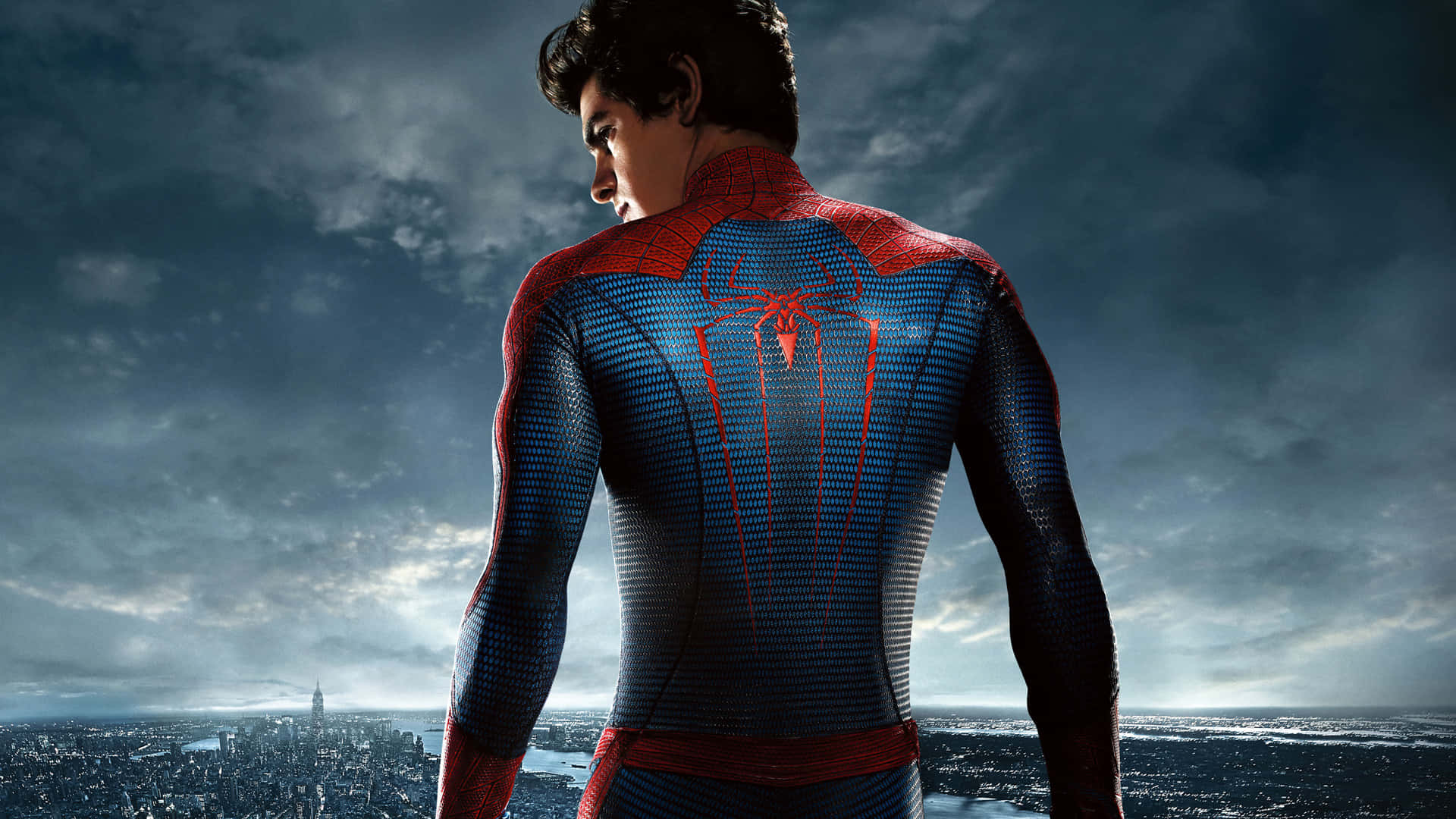 Andrew Garfield Spider Man 桌布 壁紙 — 蜘蛛人背對觀眾，俯瞰在戲劇性的多雲天空下延伸的城市。