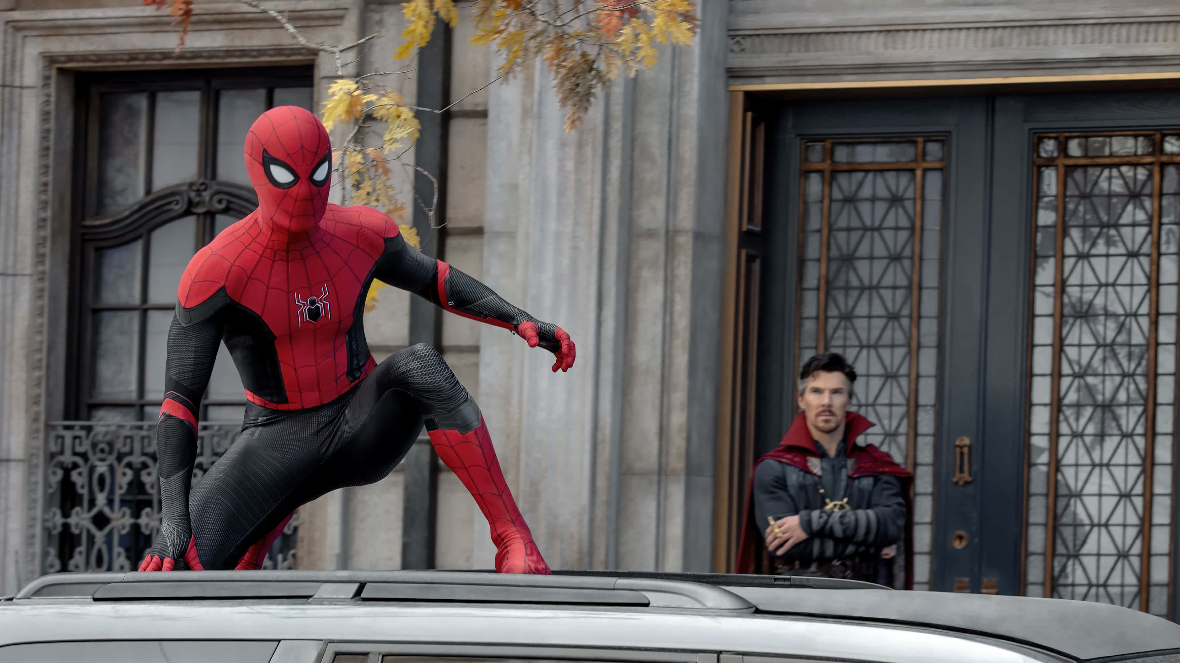 Spider Man No Way Home 桌布 壁紙 — 蜘蛛人蹲在石建築物前的車頂上，奇異博士從門口觀看。