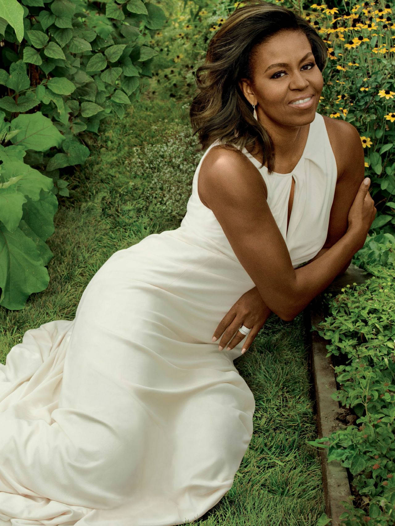 Michelle 桌布 壁紙 — 蜜雪兒·歐巴馬在鬱鬱蔥蔥的花園中穿著優雅的白色連衣裙，跪著溫暖地微笑。