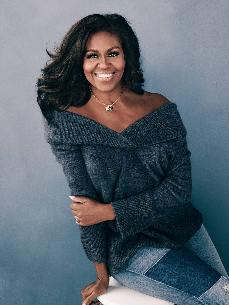 Michelle 桌布 壁紙 — 蜜雪兒·歐巴馬穿著灰色露肩毛衣和牛仔褲，在柔和的藍色工作室背景下溫暖地微笑。