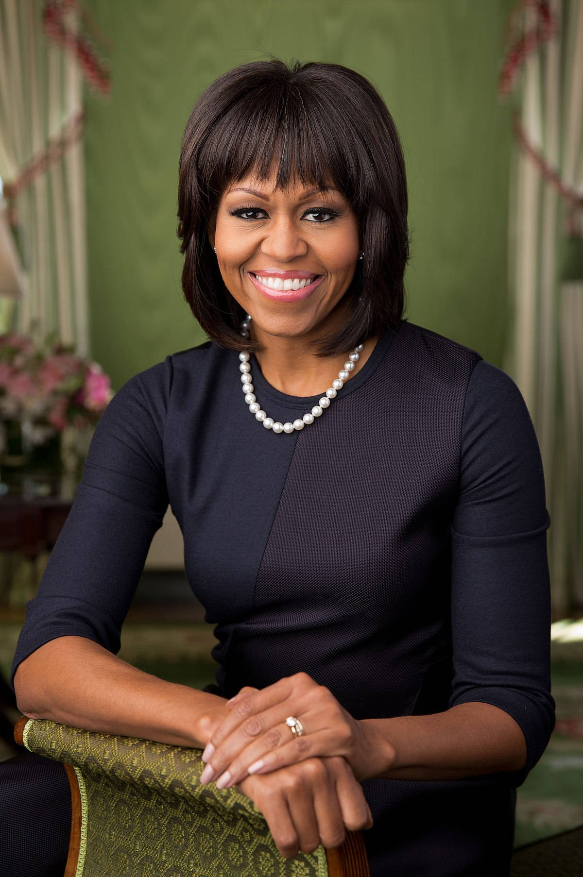 Michelle 桌布 壁紙 — 蜜雪兒·歐巴馬身穿深海軍藍連衣裙，戴著珍珠項鍊，坐在優雅的綠色房間裡，溫暖地微笑。